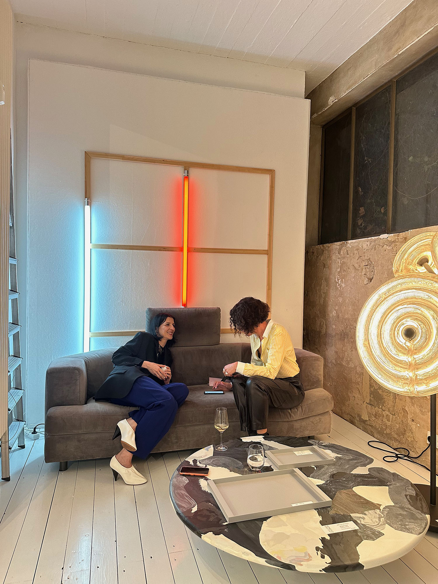 Interview im Salon des Amateurs. Mans sieht die DJ Yasmina Dexter und Jourmalistin auf einer Couch, im Hintergrund eine Leuchtenröhren-Installation.