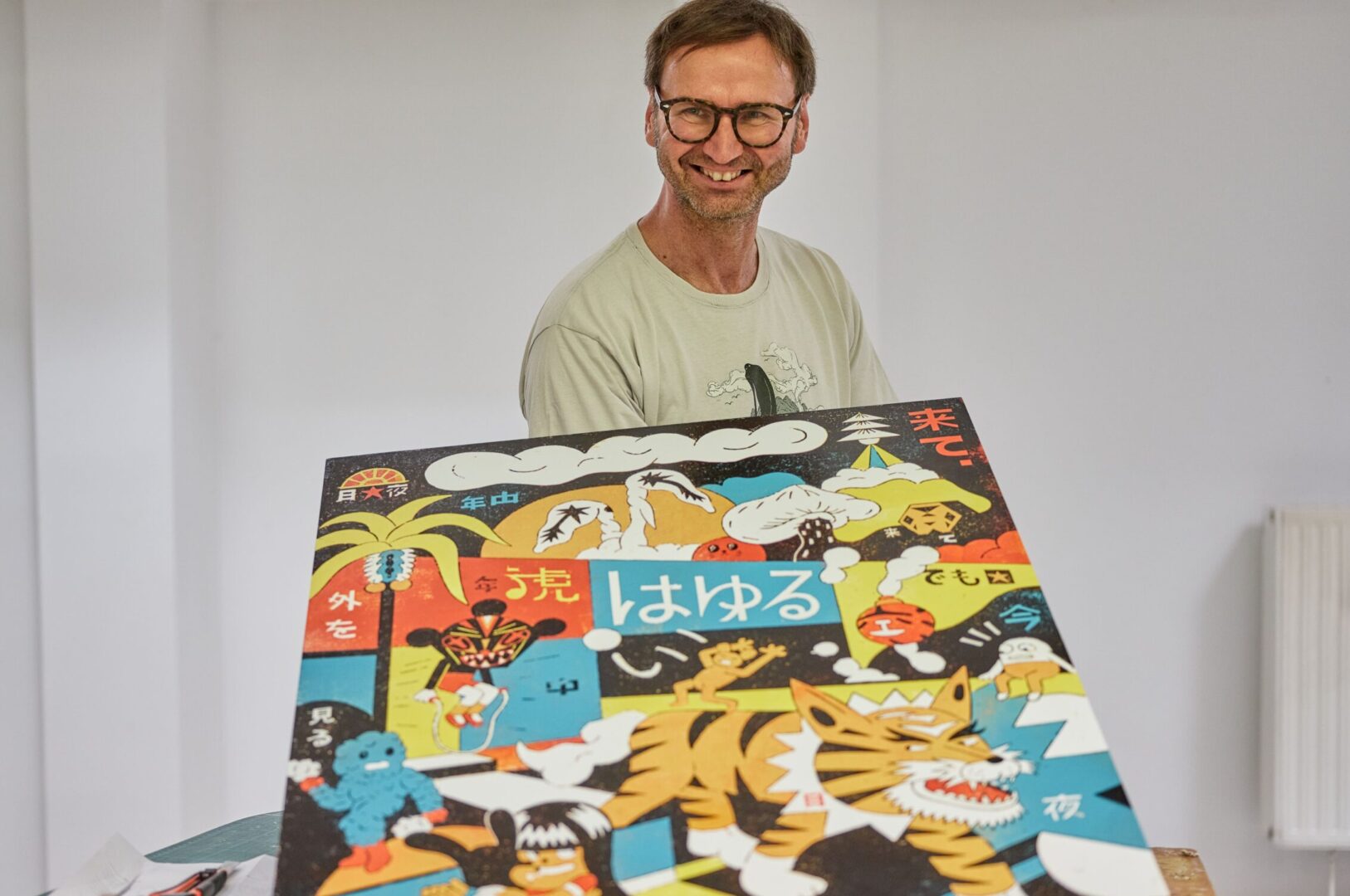 Der Düsseldorf Künstler Roman Klonek mit einem seiner Holzschnittdrucke. Das Motiv besteht aus plakativen Farben und Comic-inspirierten Figuren.