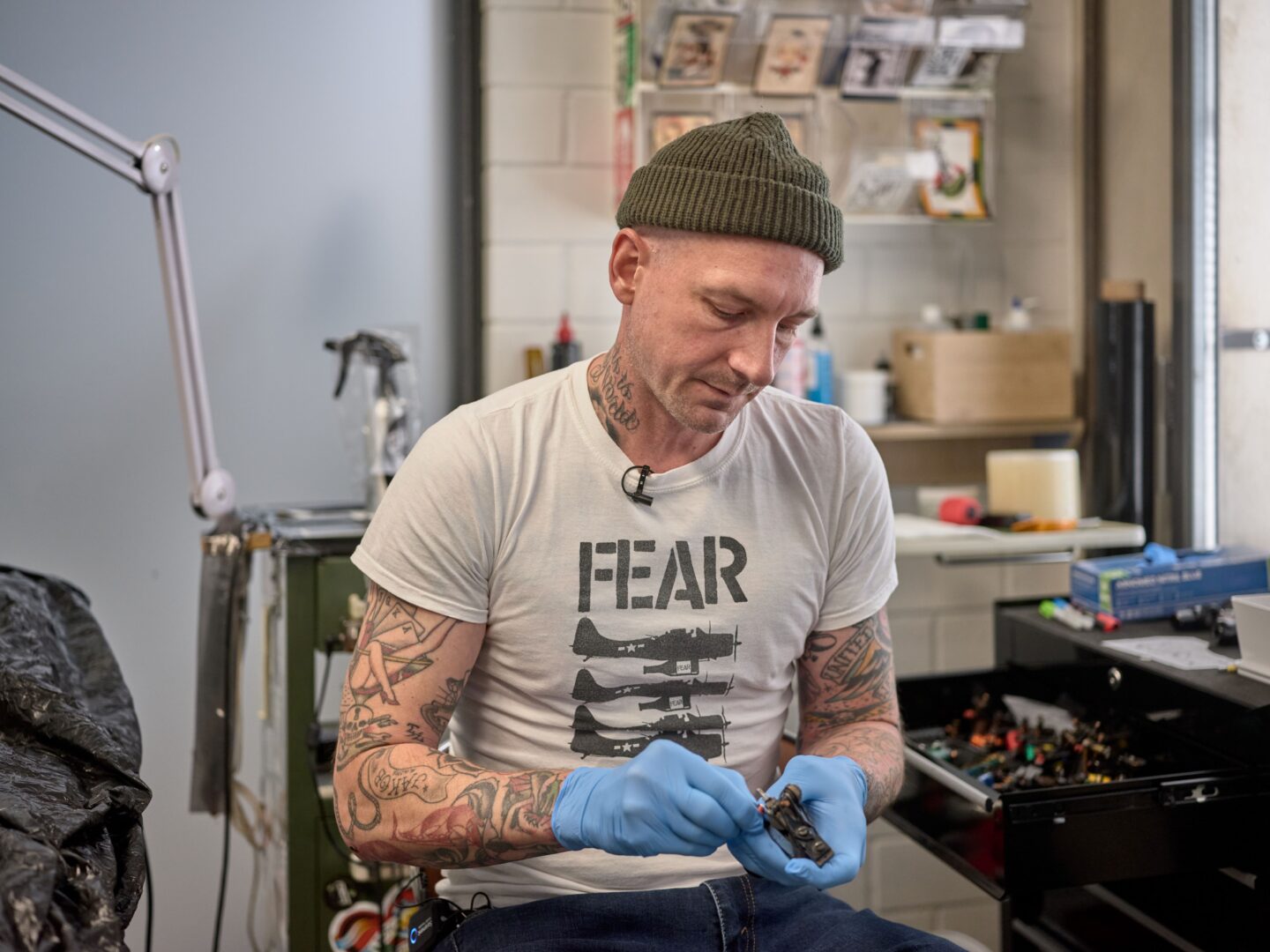 Tattoo Artist Till Pulpanek bereitet sich aufs Tätowieren vor, er trägt blaue Gummihandschuhe und desinfiziert ein Werkzeug.