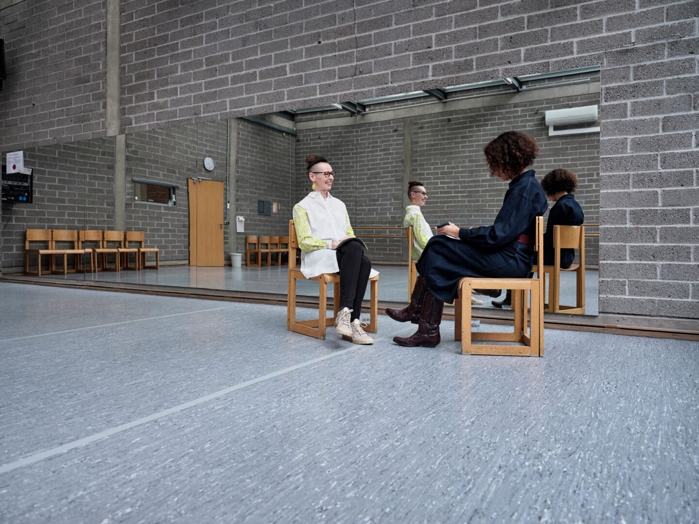 Zwei Frauen auf Stühlen vor einem Spiegel in einem Tanzstudio.