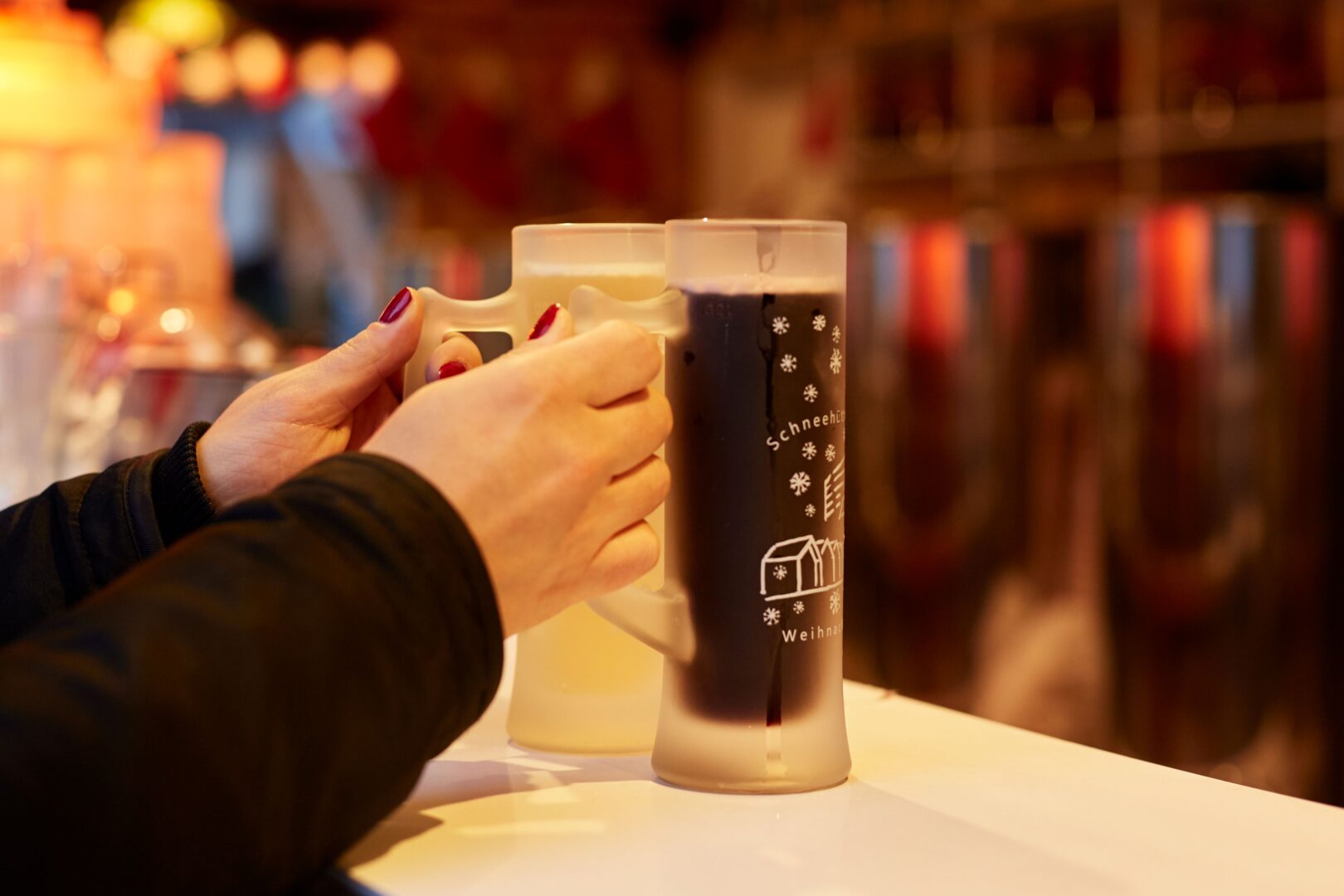 Zwei Hände halten Henkelgläser mit weißem und rotem Glühwein.