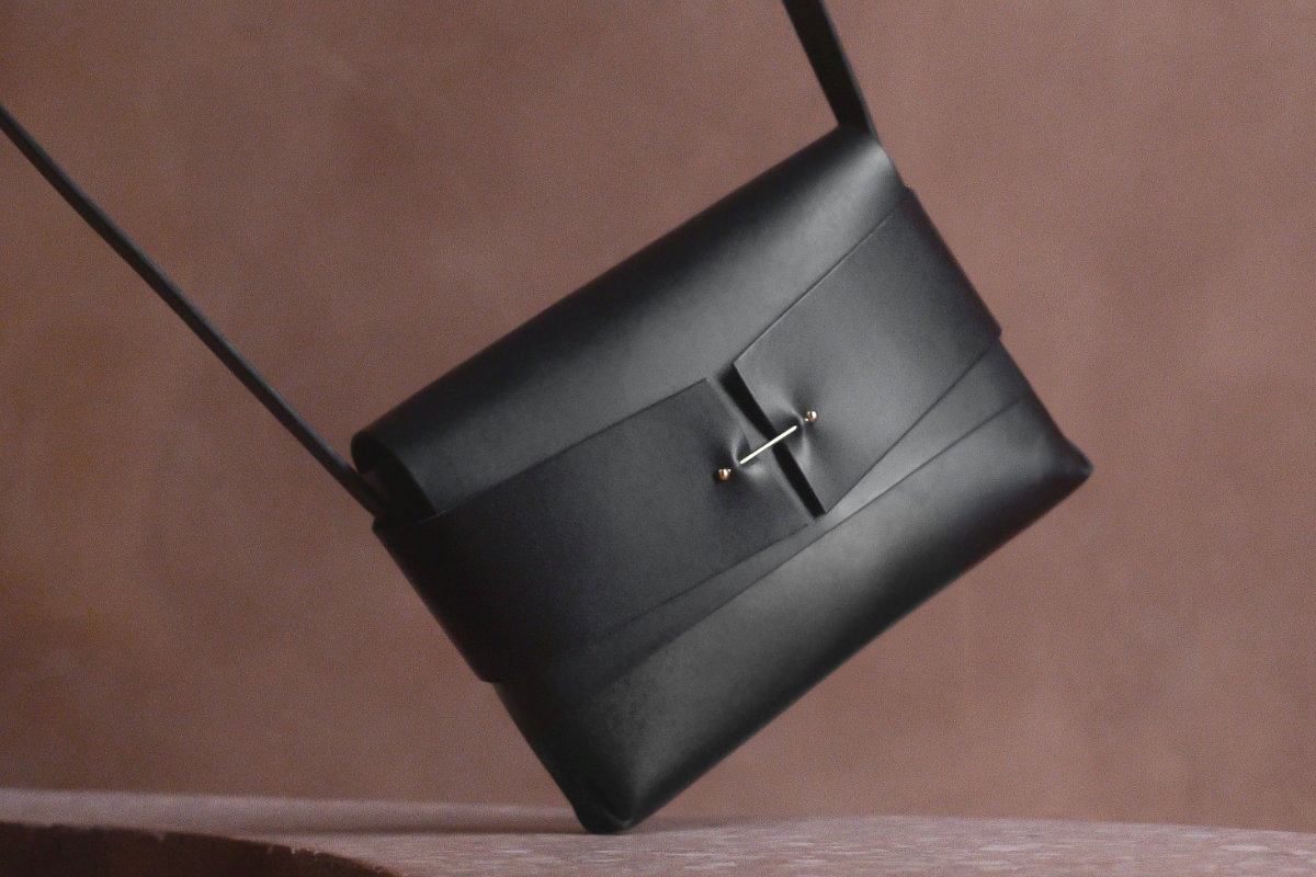 Schwarze Lederhandtasche zum Umhängen vor braunem Hintergrund.