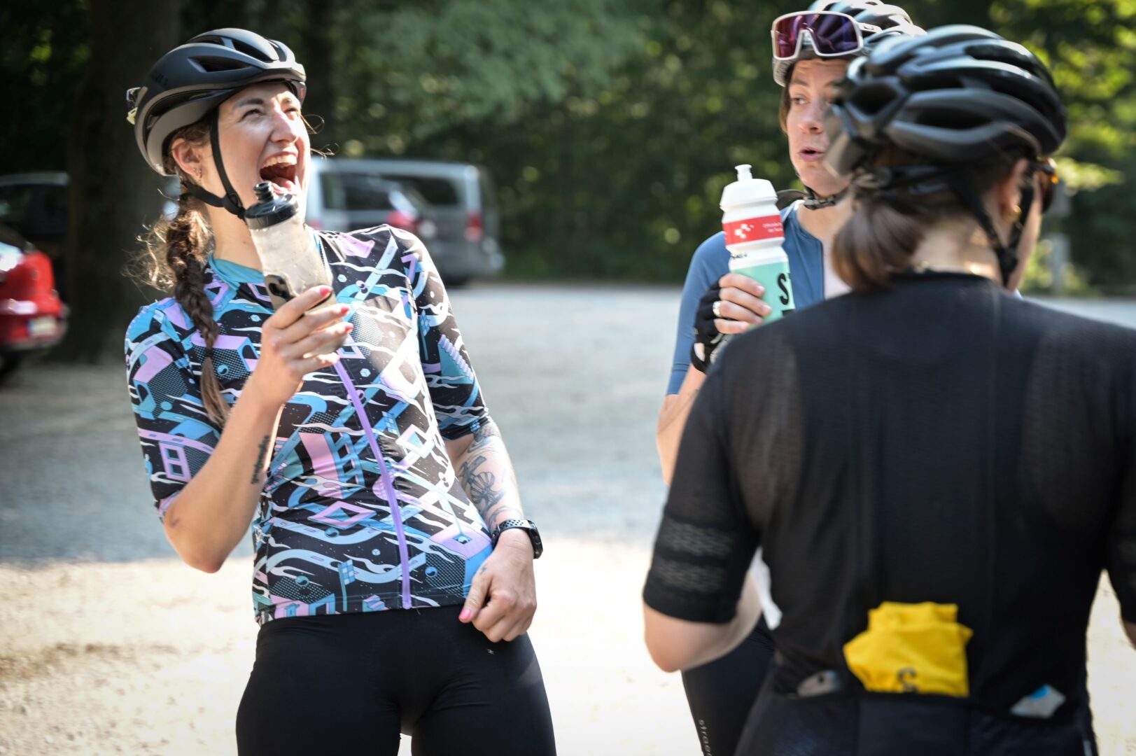 Drei Rennradfahrerinnen bei einer Pause, eine lacht fröhlich.