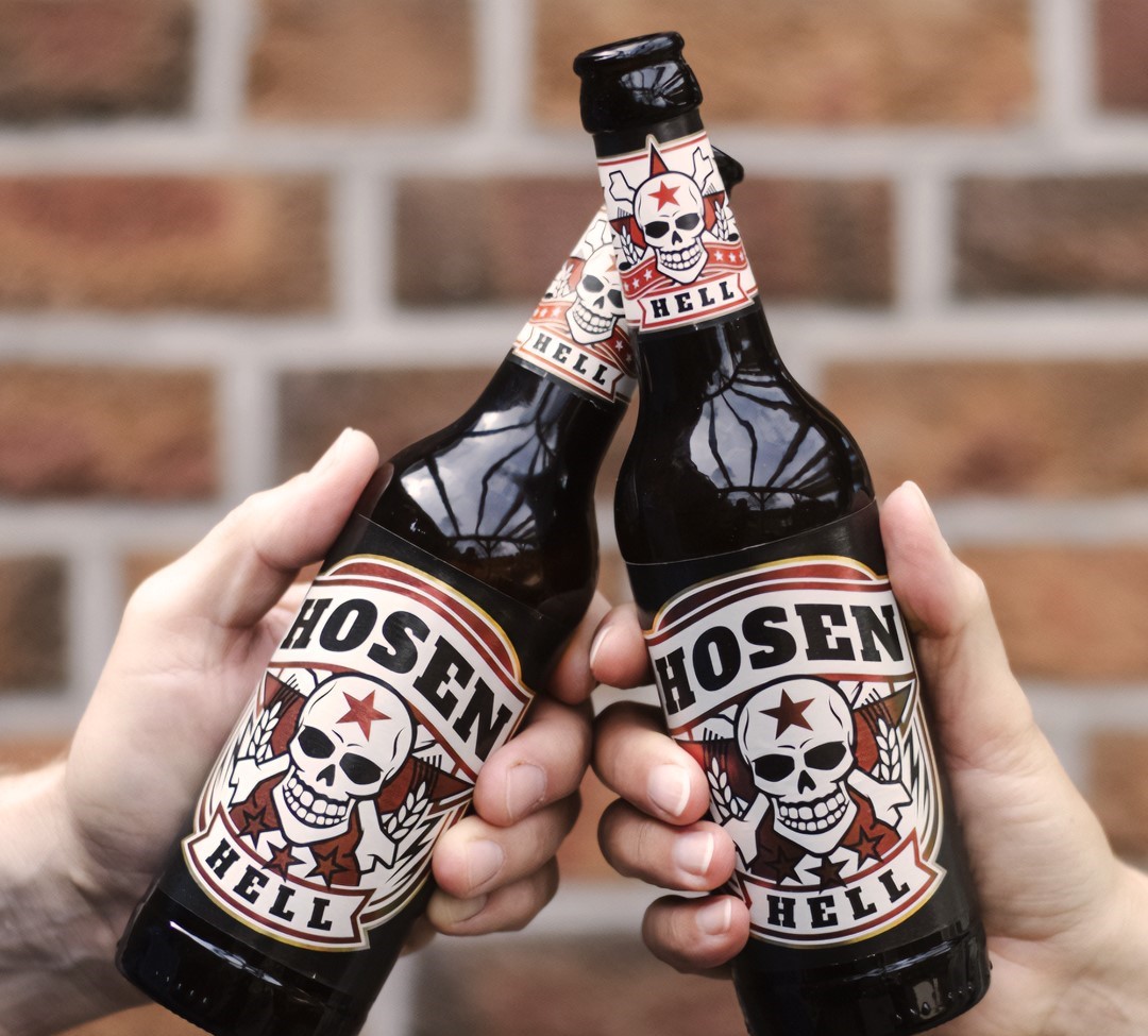 Zwei Hände im Anschnitt stoßen mit Flaschenbier Hosen Hell an.