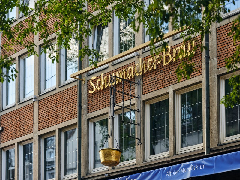 Schumacher-Brauerei, man sieht die Schrift am Backsteingebäude durch Zweige.