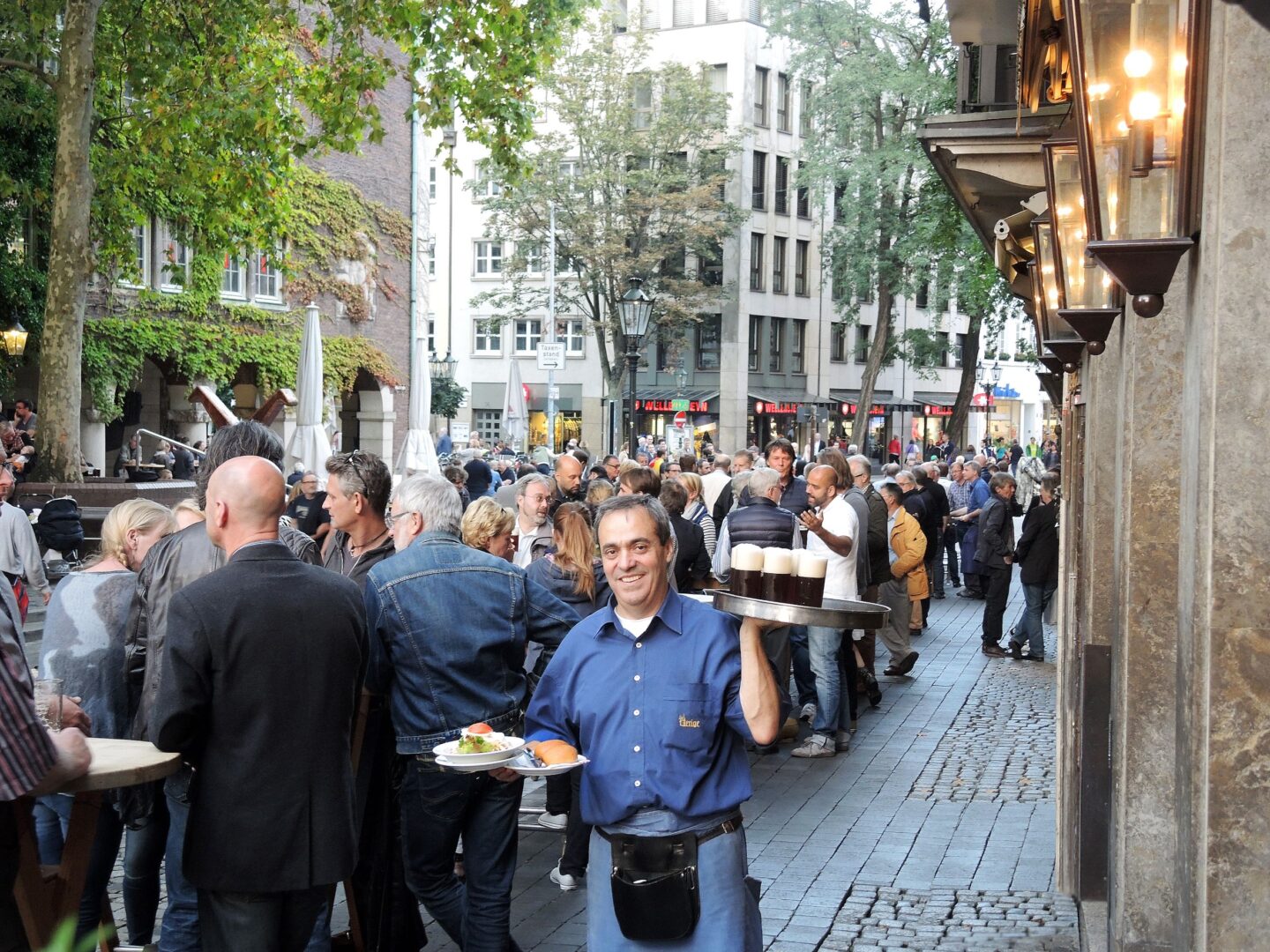 Köbes, Düsseldorfer Brauhaus-Kellner, trägt draußen ein Tablett mit Bier.