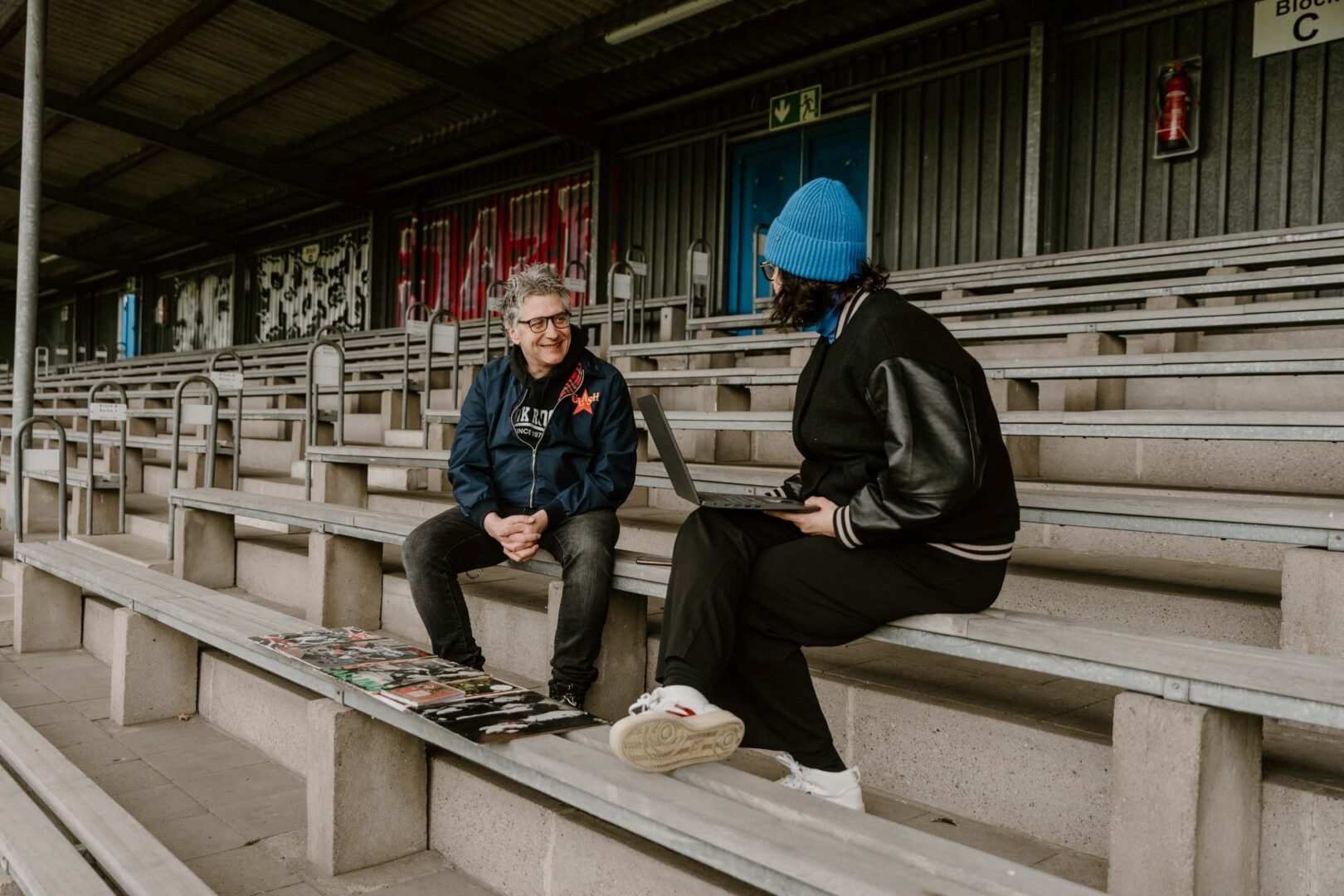 Marcus Haefs spricht mit Autorin Katja Vaders, beide sitzen auf der Tribüne. 