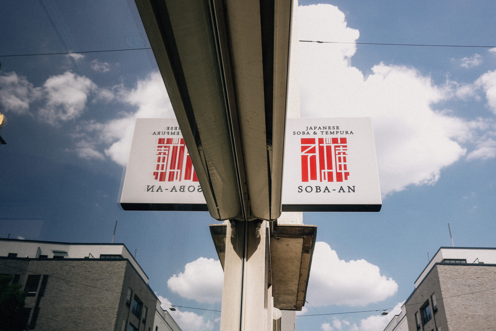 Das Schild des Restaurants Soba-An von schräg unten gegen blauen Himmel mit weißen Wolken aufgenommen.