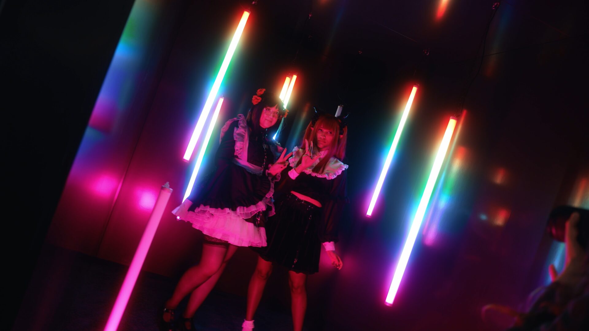 DoKomi 2023, 2 Cosplayerinnen in eine,m dunklen mit bunten Neonröhren beleuchteten Raum.