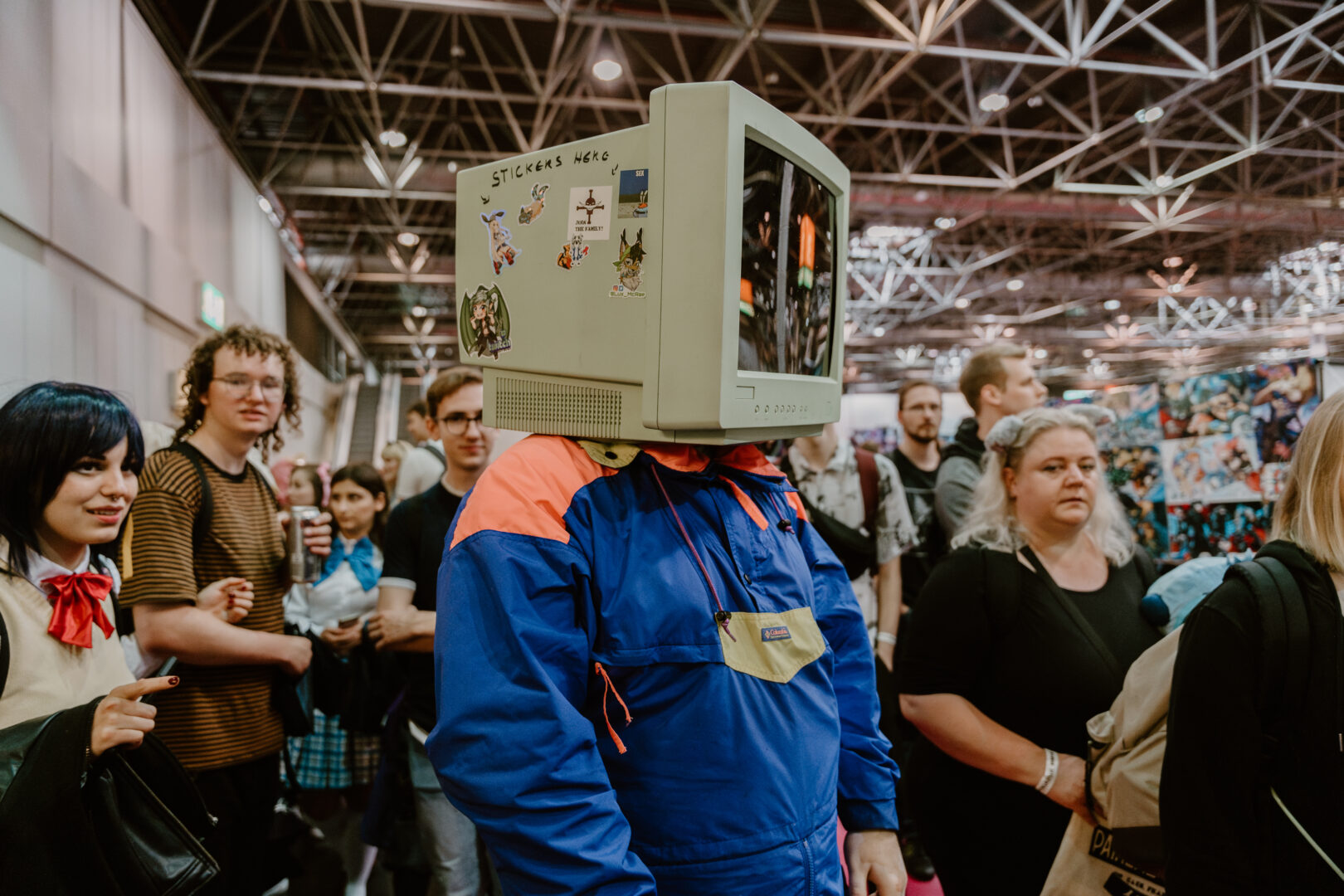 Mann in blauem Iverall, der einen alten Computermonitor über dem Kopf trägt, wie einen Helm.