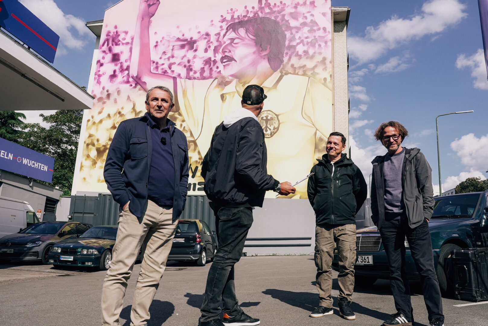Urban Art: Das Wandgemälde von Klaus Allofs, davor stehen vier Männer u.a. Klaus Allofs und Klaus Rosskothen.