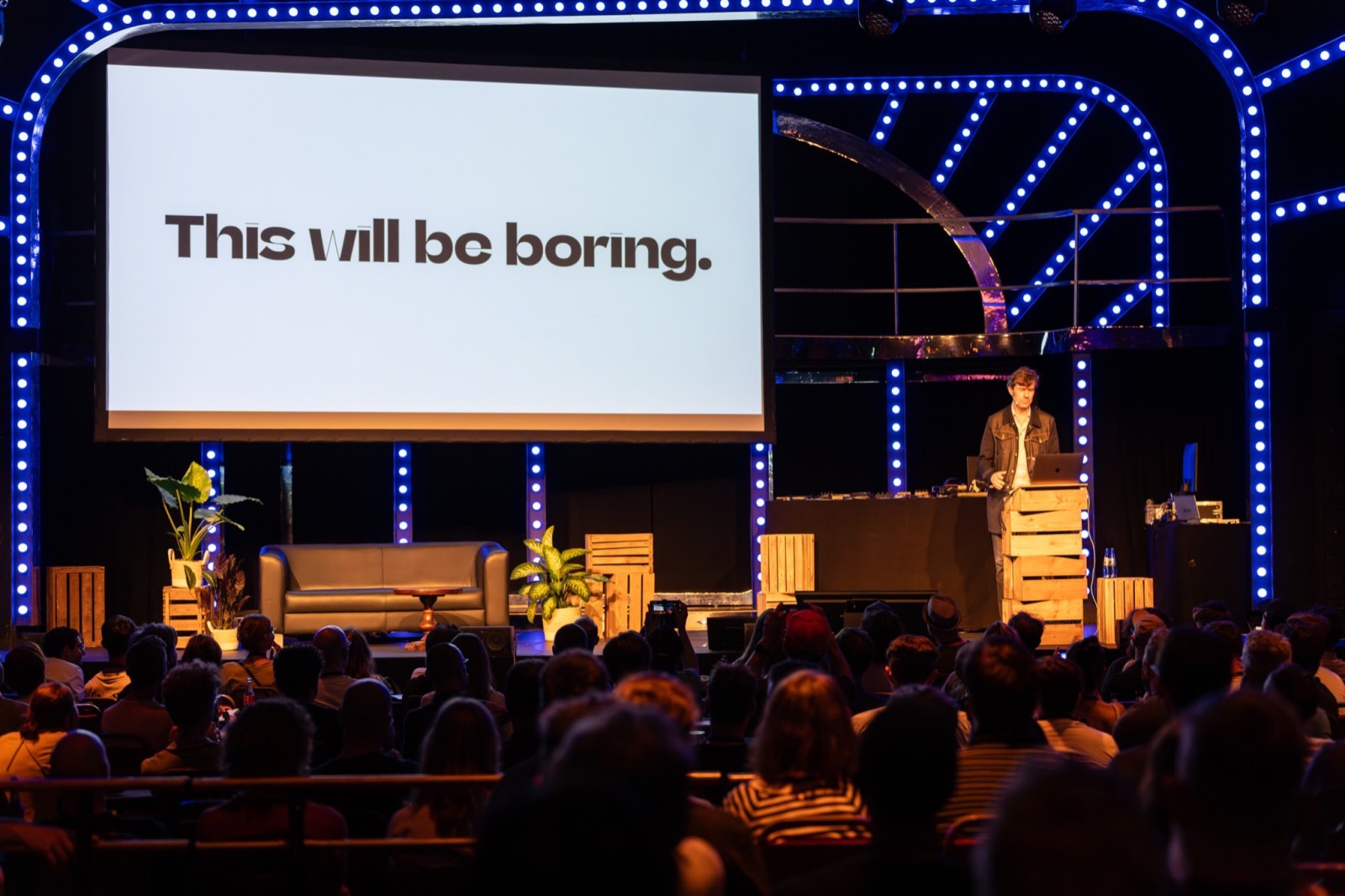 Stefan Sagmeister auf der Bühne bei Beyond Tellerrand. Man sieht Publikum von hinten, auf einem Bildschirm steht: This will be boring.