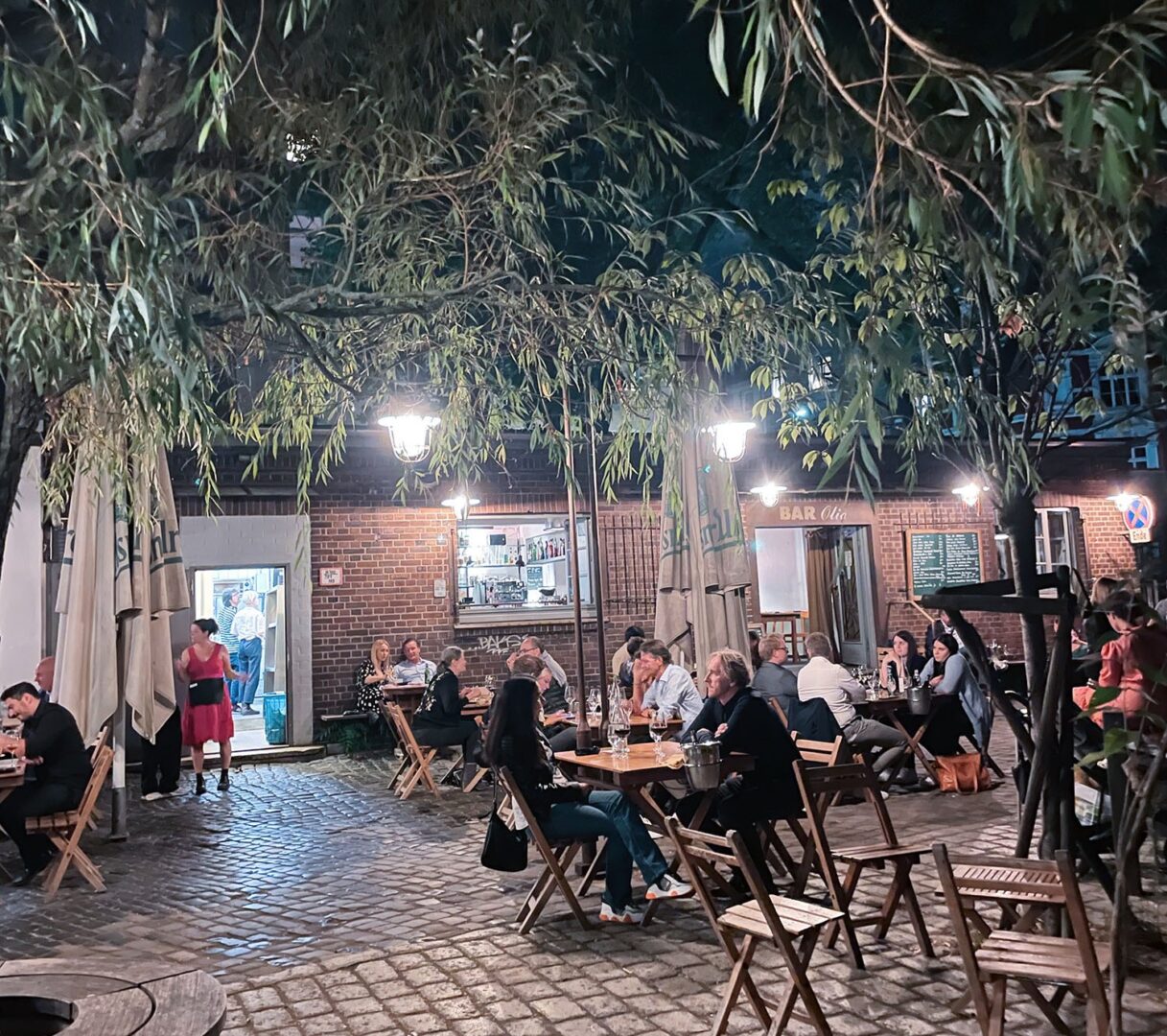 Summer Vibes auf der Terrasse der Bar Olio, man sieht die Terrasse vor dem Olio, ein Backsteingebäude bei Nacht.