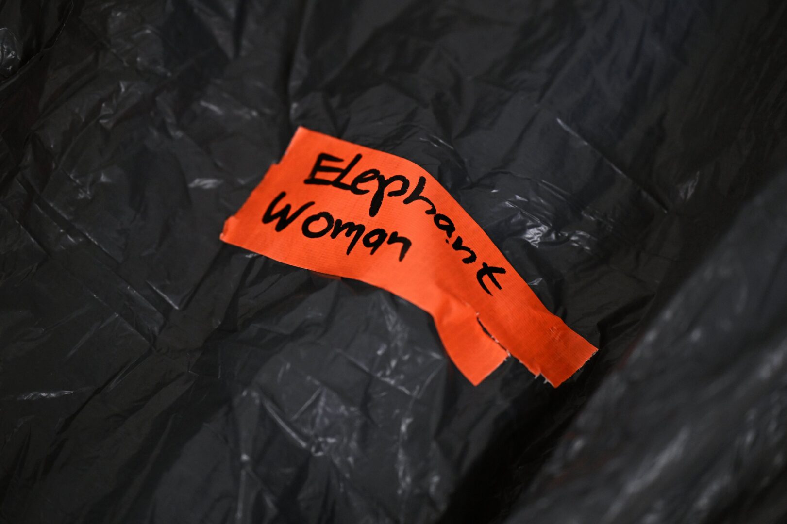 Ein roter Aufkleber, auf dem "Elephant Woman" steht, klebt auf schwarzem Verpackungsmaterial.