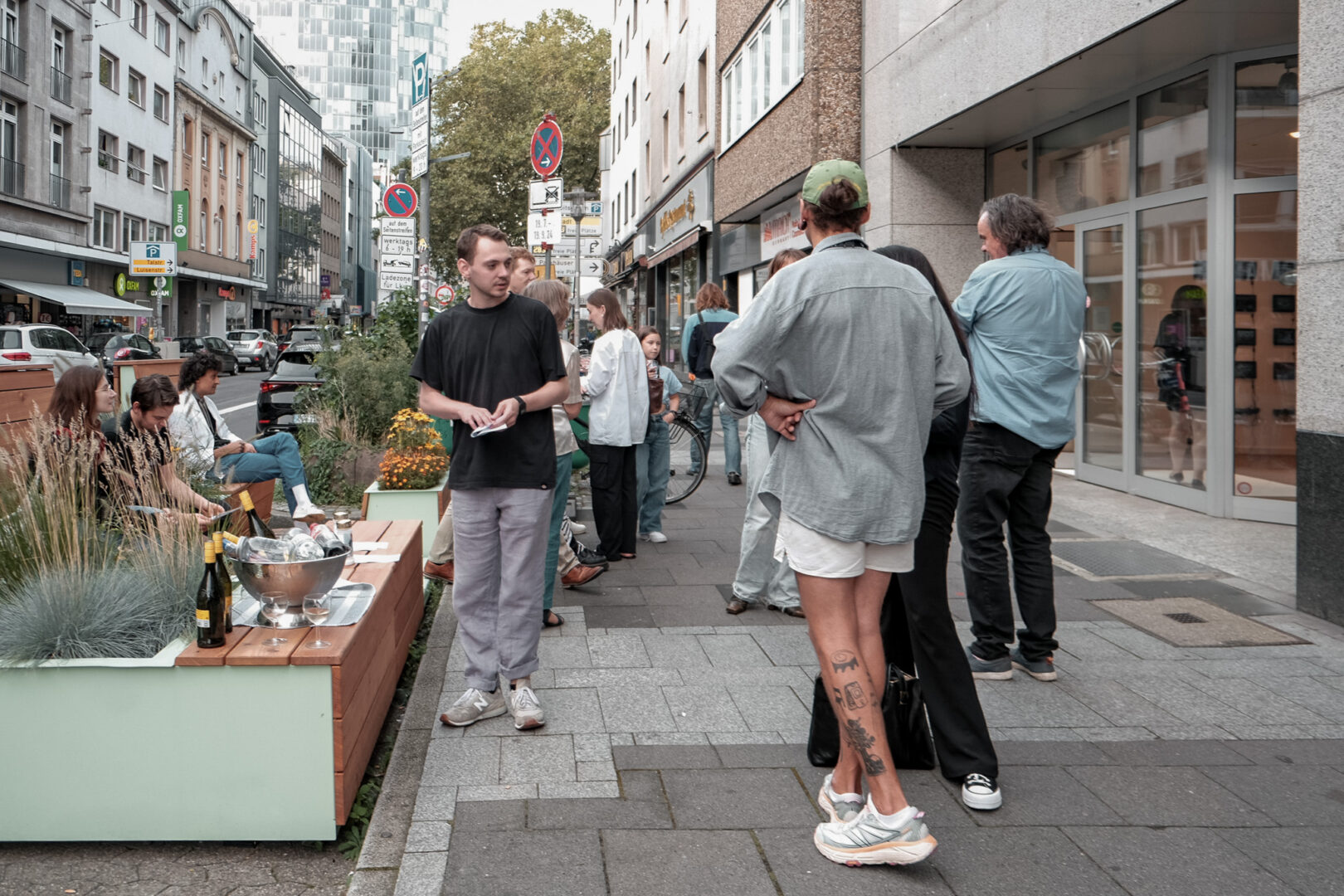 Parklet vor der Offspace-Galerie an der Friedrichstraße und viele Menschen, die sich darum herum aufhalten, reden und Sekt trinken.