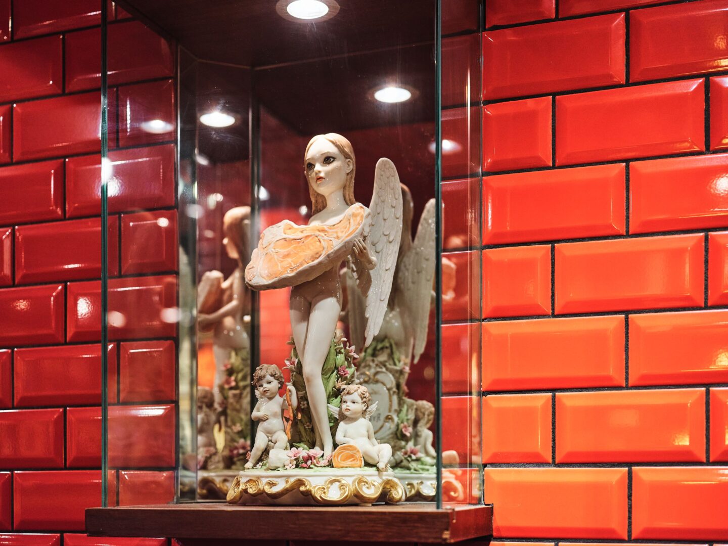 Porzellanfigur hinter Glas: eine eflenartige Figur hält ein großes, rohes Steak in den Händen.