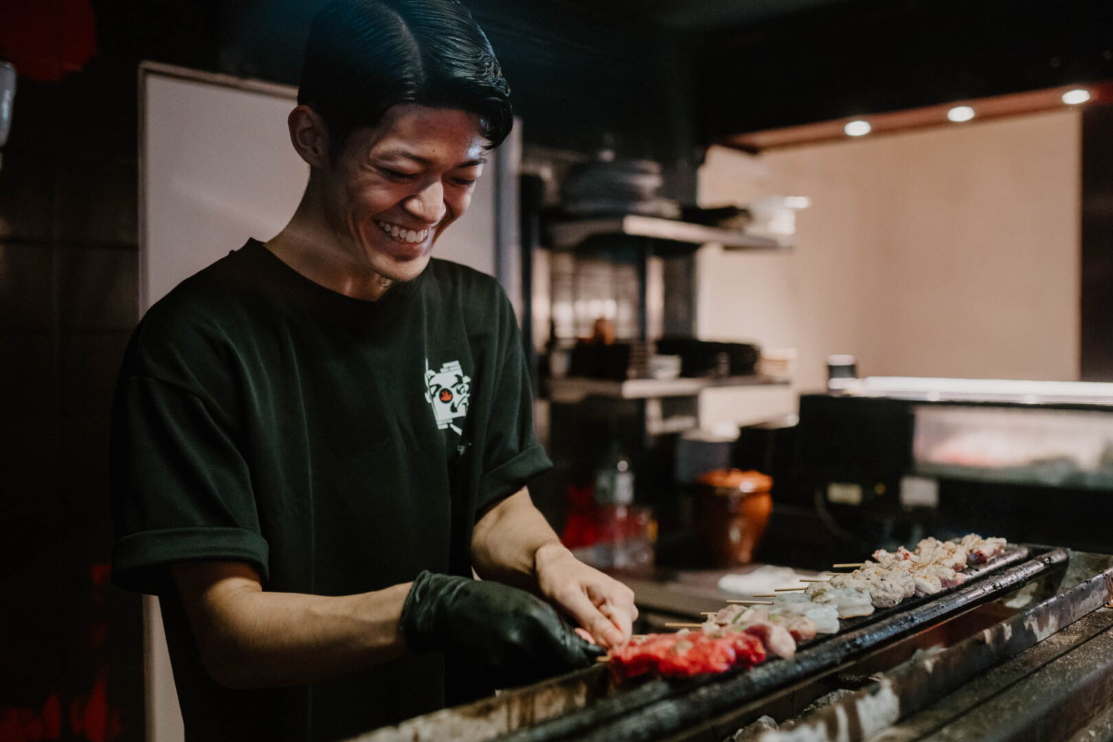 Man sieht einen japanischen Koch am Holzkohlegrill arbeiten.