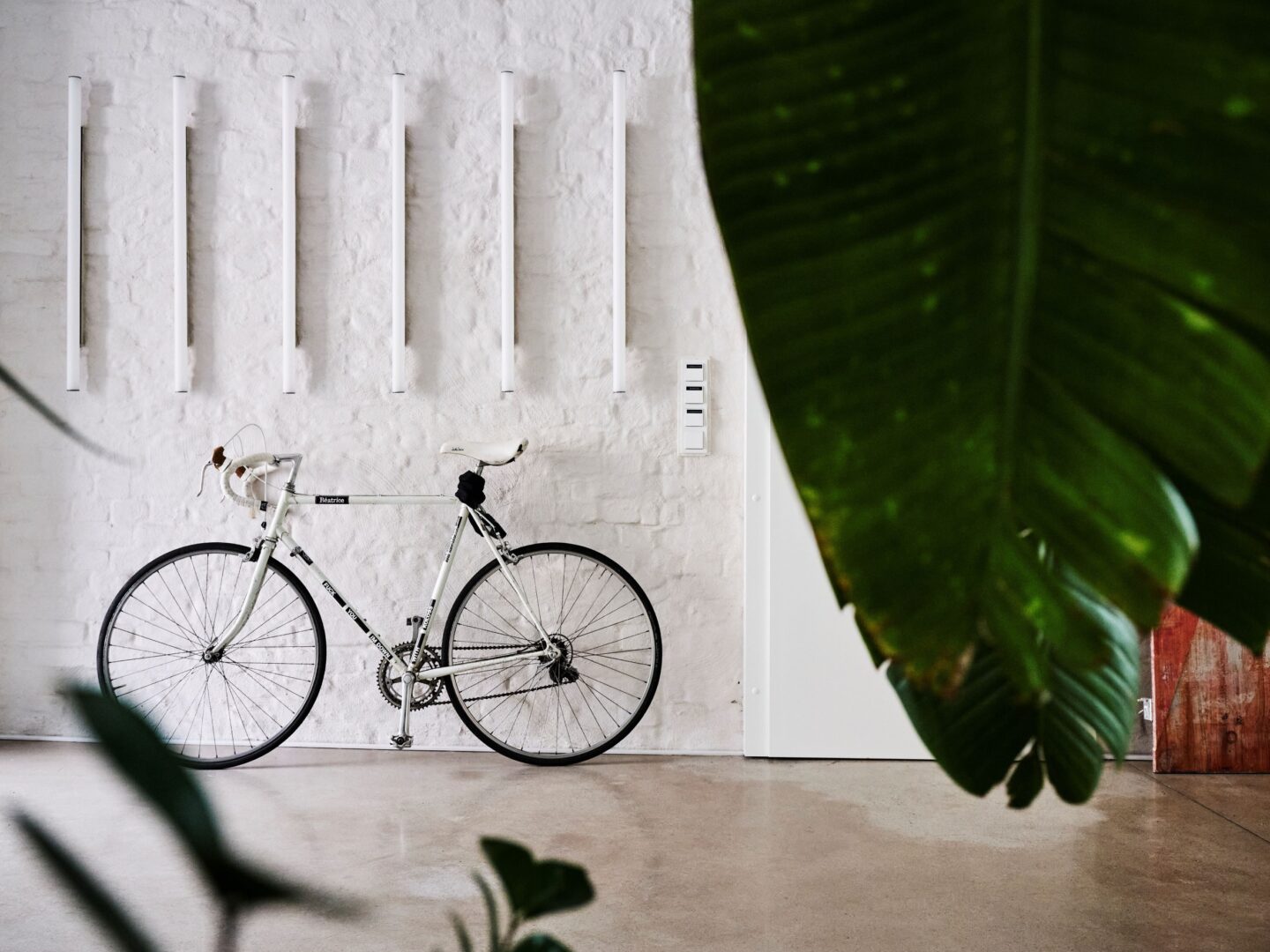 Weißes Rennrad lehnt an eine weiße Backsteinwand.