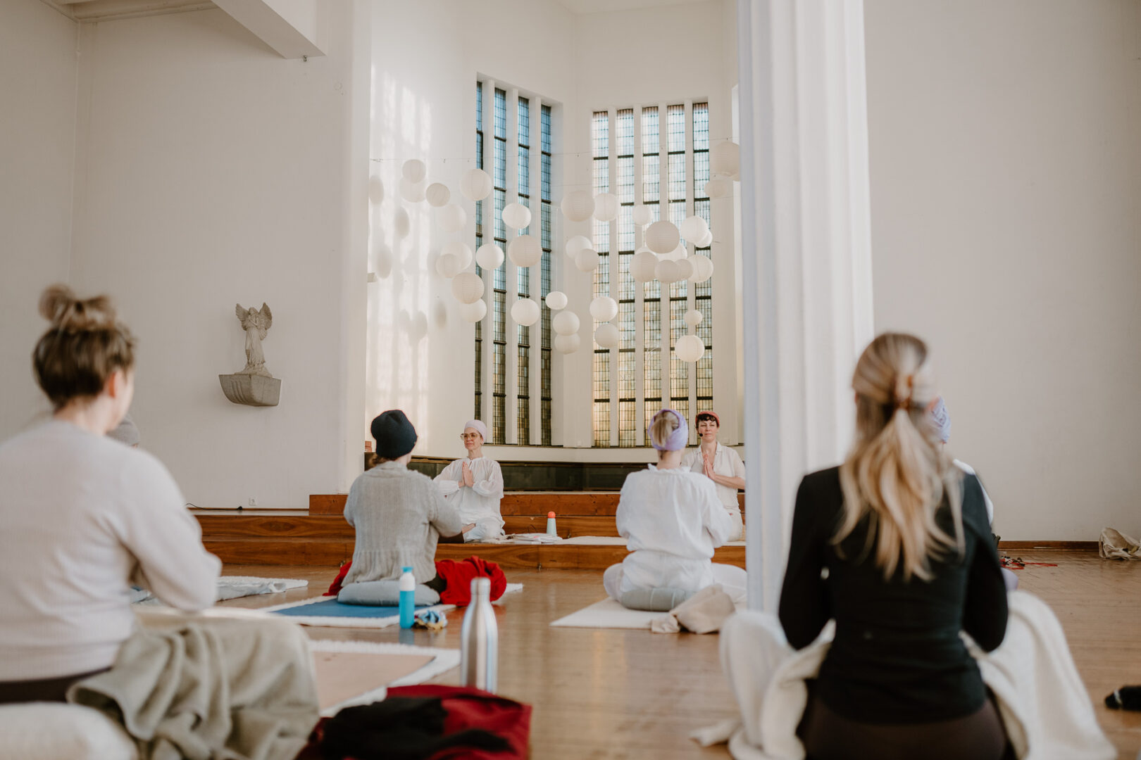 Man sieht eine Yogaklasse und vorne die Yogalehrerin