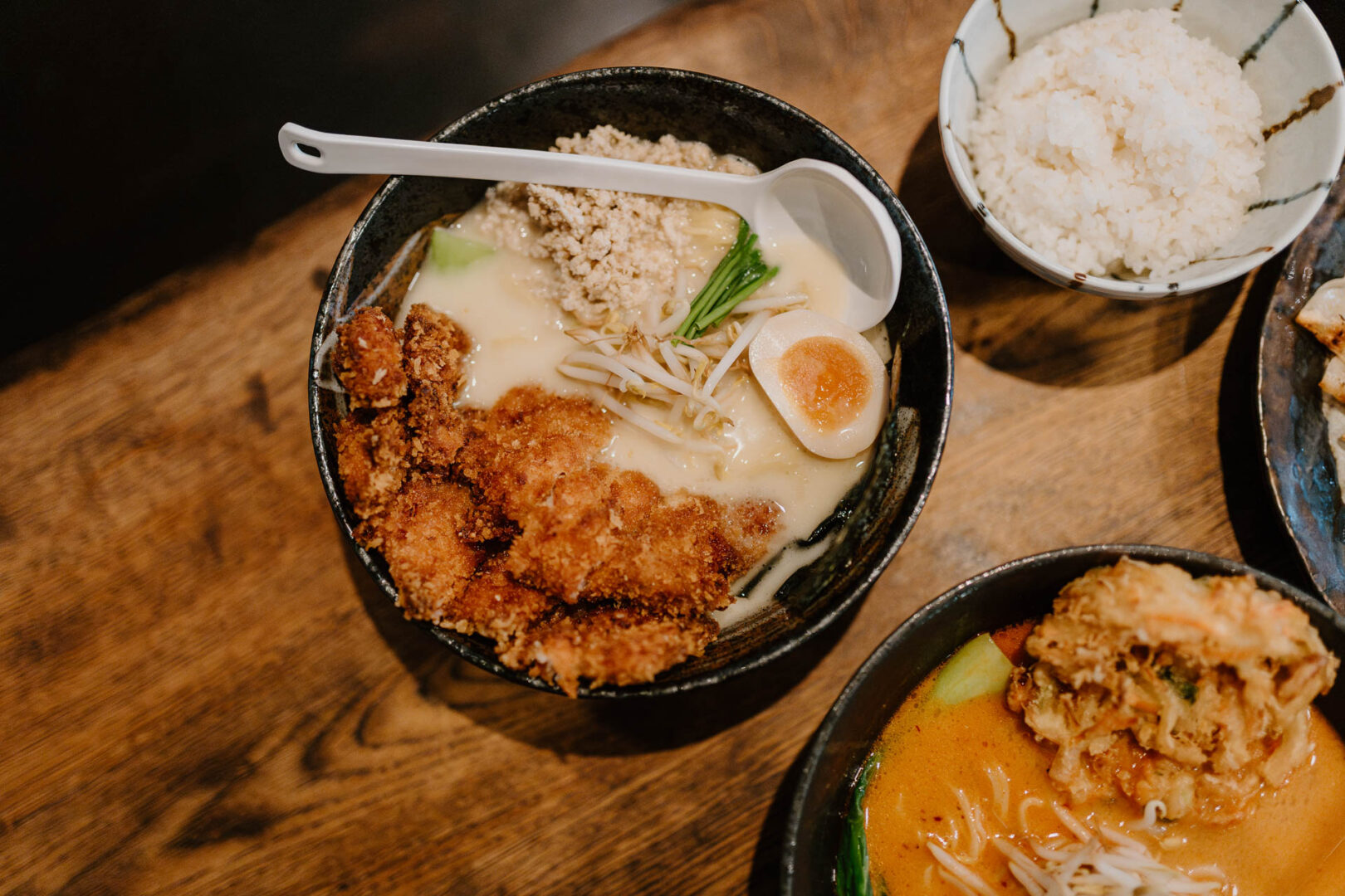Man sieht den Ausschnitt eines Holztisches von oben. Auf dem Tisch stehen Ramen.