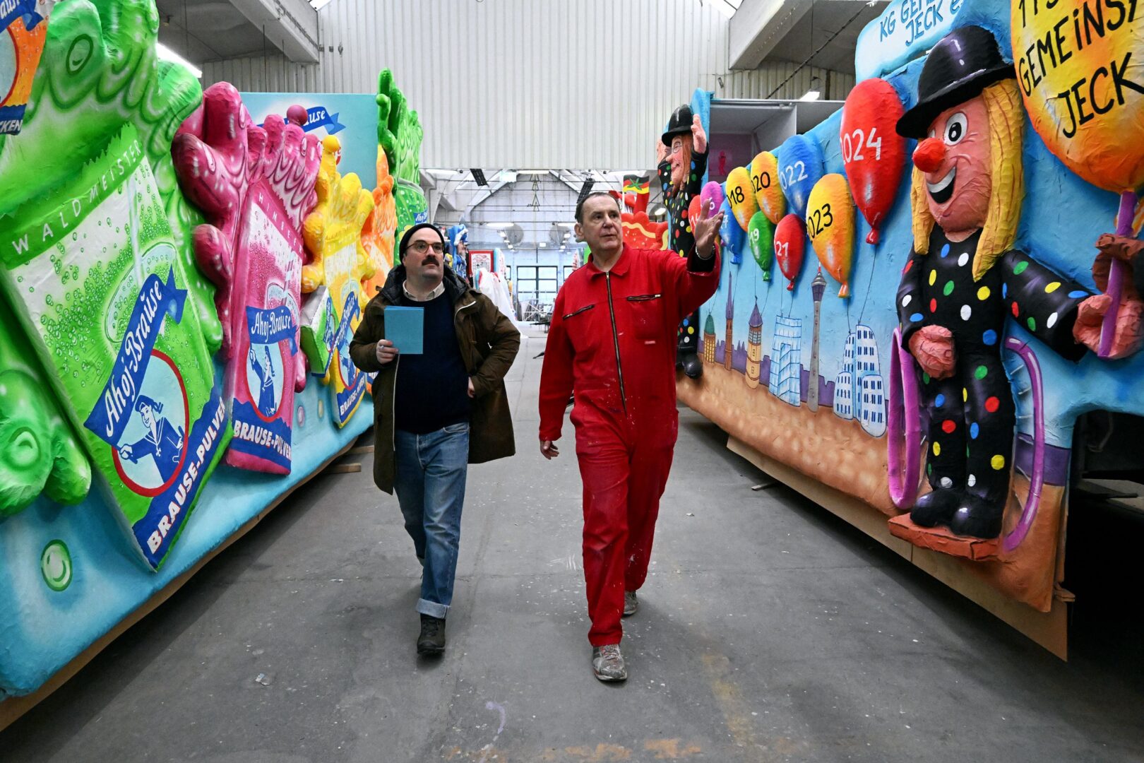Autor Clemens Henle (links) und Jacques Tilly gehen gemeinsam durch die Wagenbauhalle.