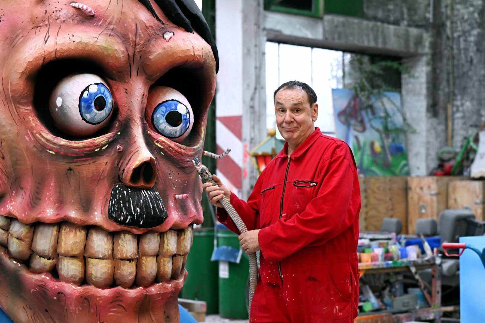 Jacques Tilly neben einer Wagenplastik: eine Art Totenkopf mit Hitlerbärtchen.