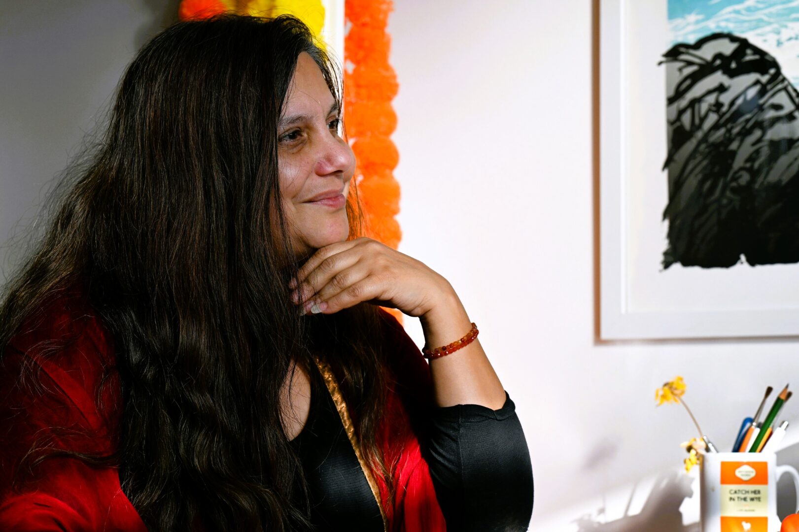 Mithu Sanyal im Profil, sie sitzt bei sich in der Küche an einem Tisch.
