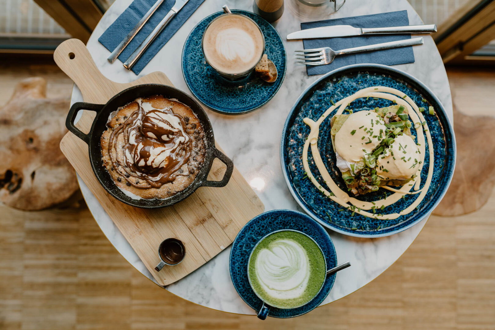 Man sieht einen gedeckten Tisch von oben mit einem grünen Matcha-Latte, Capuccino und zwei Gerichten. 