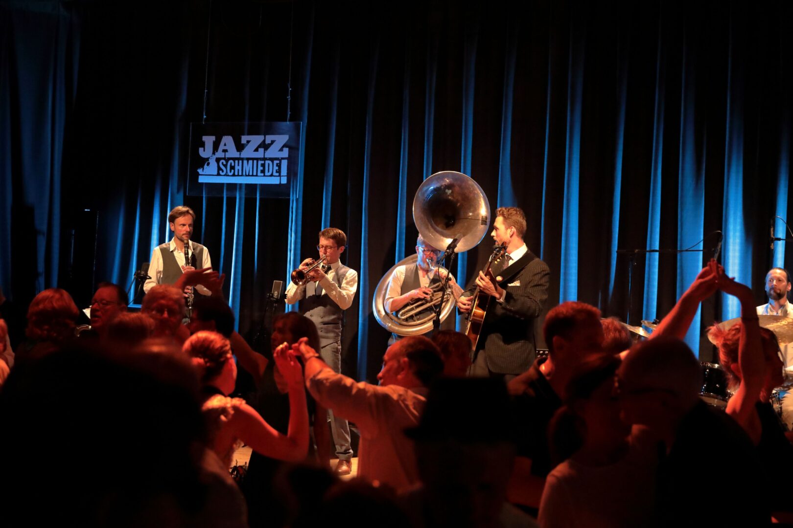 Jazz-Band auf der Bühne, im Hintergrund ist ein dunkelblauer Samtvorhang. 