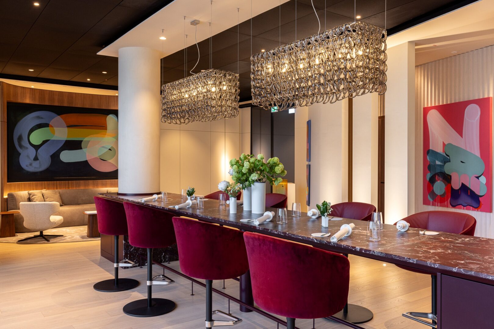 Man sieht das La Vie von innen, ein langer Tisch mit Blumen dekoriert und eingedeckt dazu dunkelrote Drehsessel. Im HIntergrund eine Bar und abstrakte Kunstgemälde.