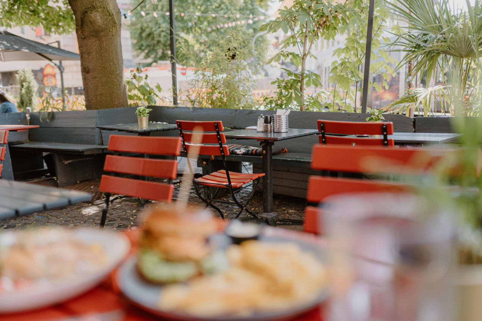 Man sieht unscharf im Vordergrund einen Teller mit einem Burger, im Hintergrund sieht man die sommerliche Terrasse des Lokals Beethoven.