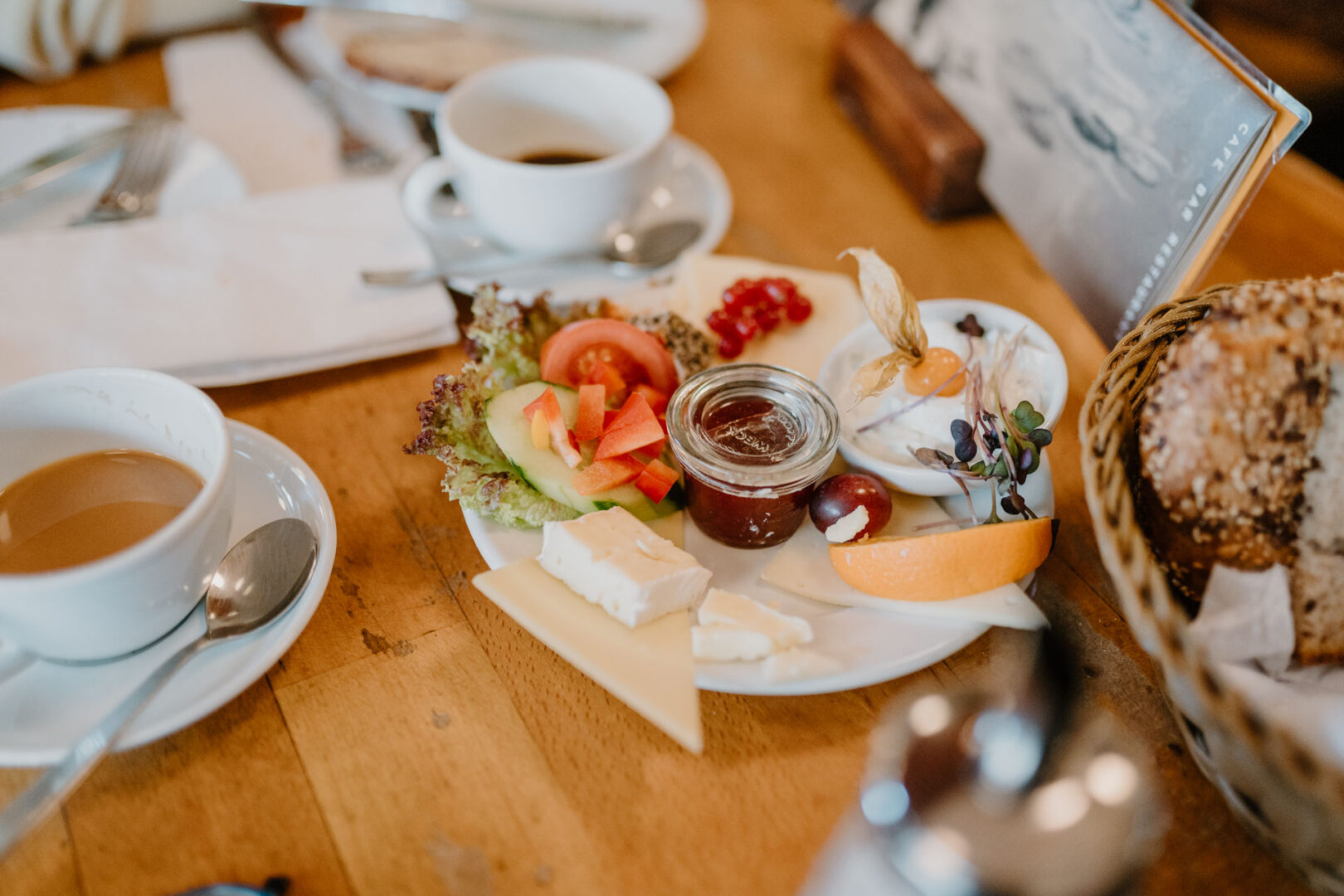 Ein Tisch mit Frühstück: Kaffeetasse, Teller mit Konfitüre, Käse und Butter.