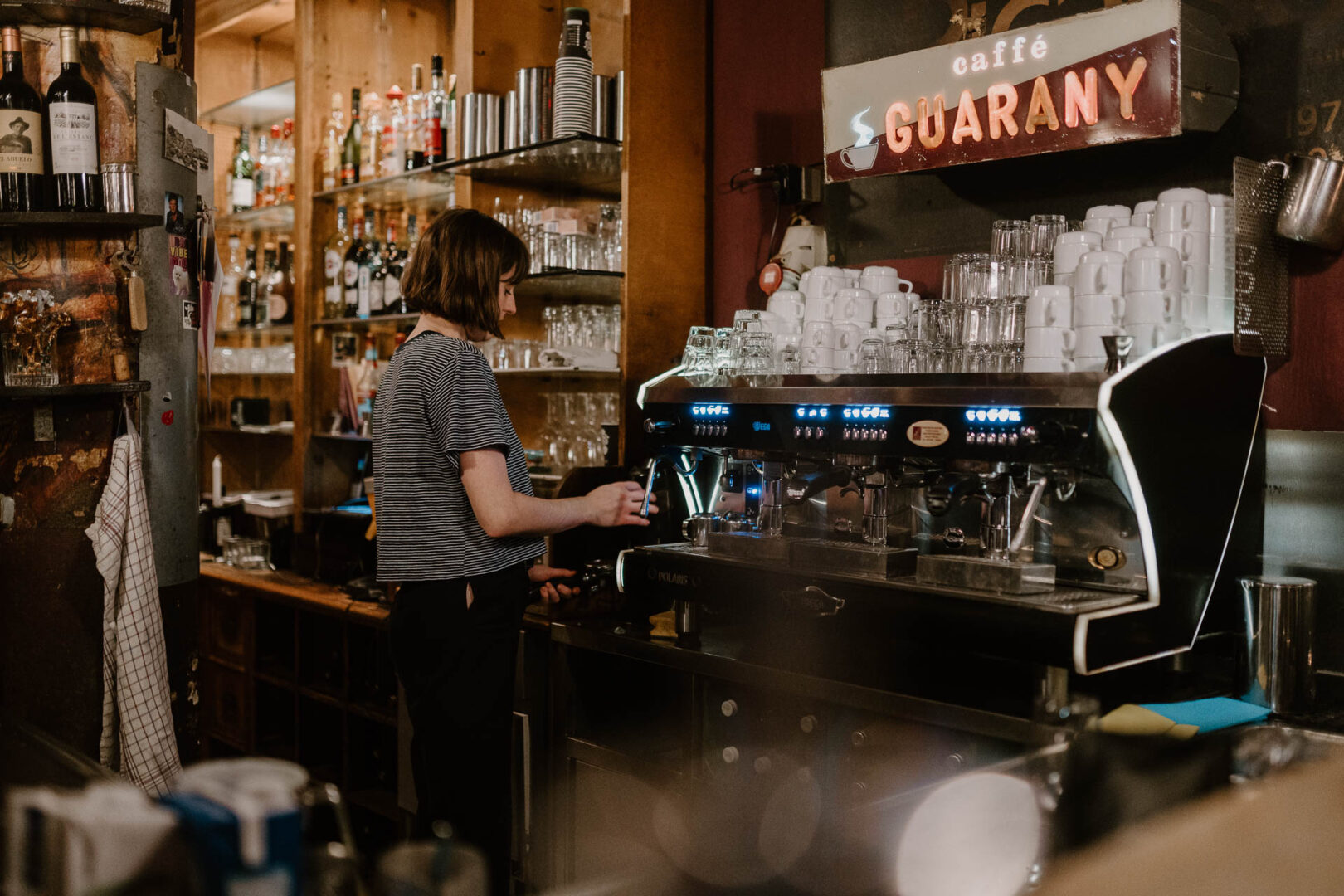 Man sieht eine Kellnerin hinter der Bar einen Kaffee zubereiten.