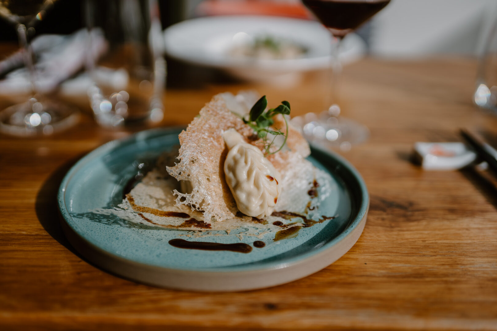 Man sieht einen Holztisch mit einem türkisgrünen Teller, auf dem Dumplings angerichtet sind.