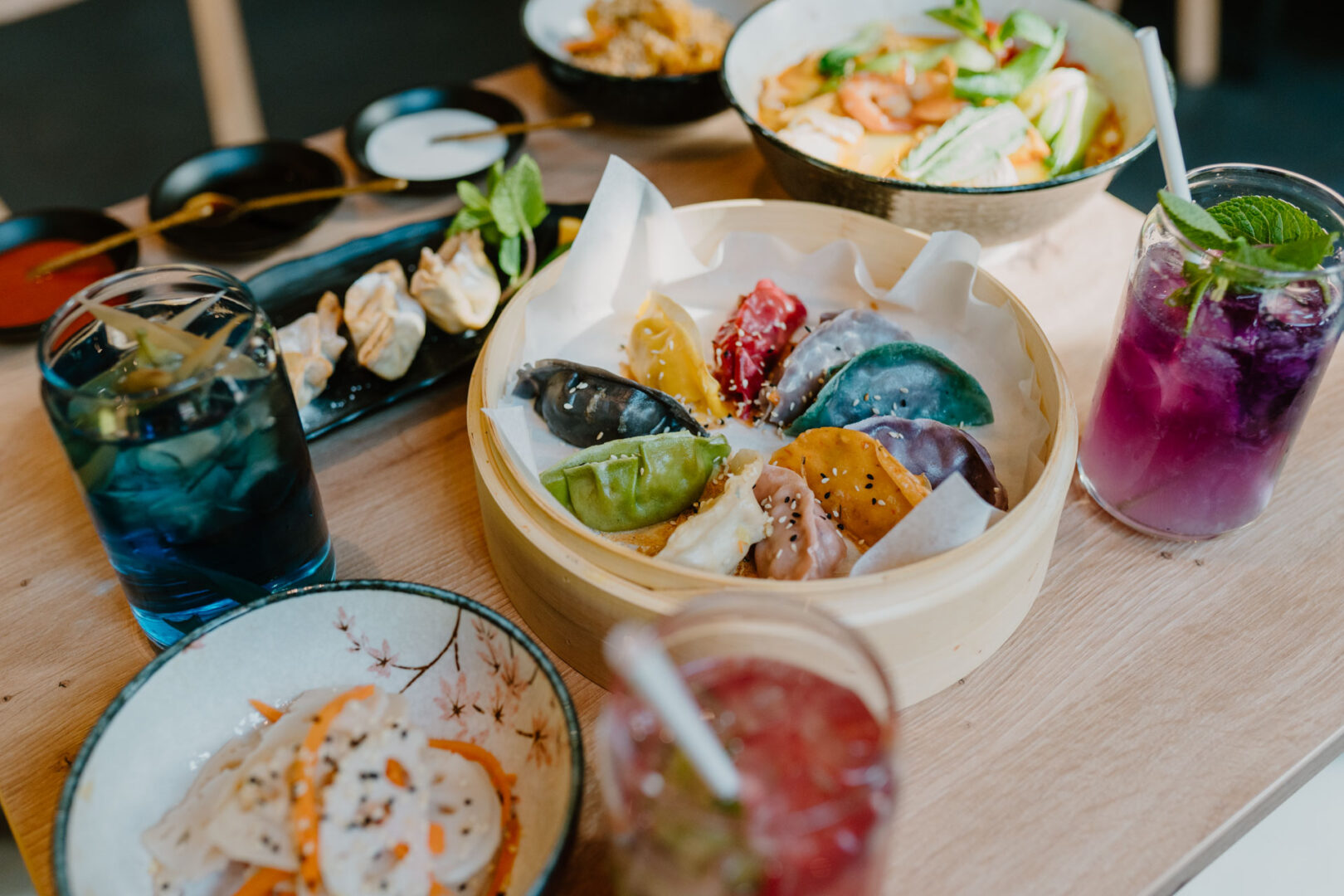 Man sieht einen gedecken Tisch in dem Restaurant Mama Gyoza. In der Mitte ein Bambuskorb voller bunt eingefärbter Gyoza in Blau, Rot, Grün, Gelb, Orange und Schwarz.