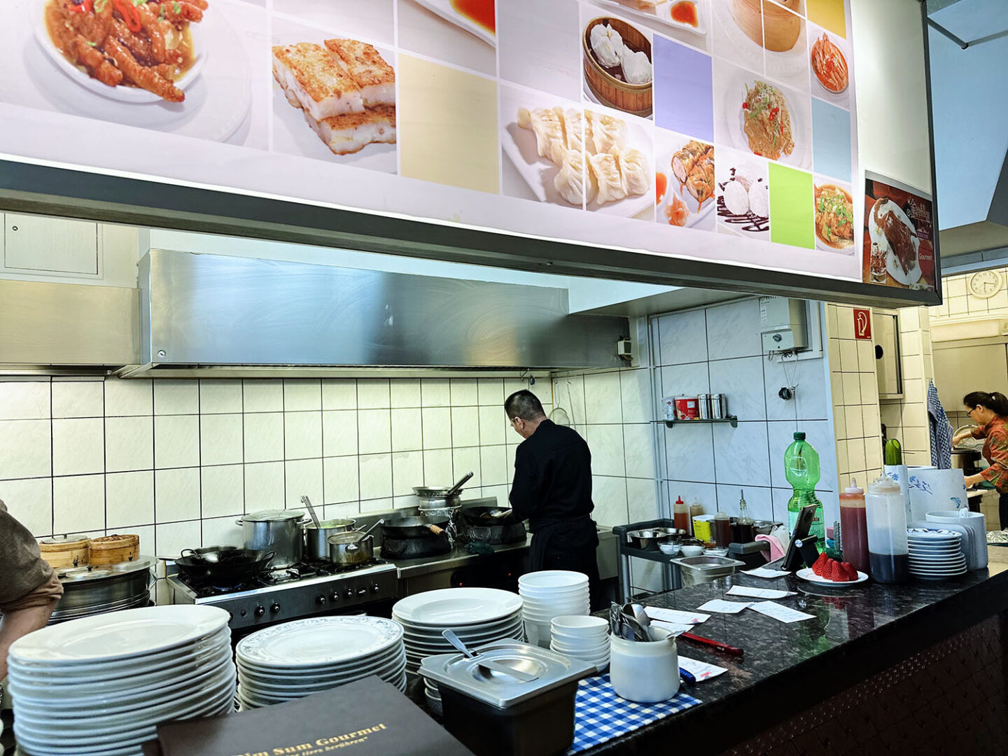 Man blickt in die offene des Dim Sum Gourmet und sieht vorne die Ablagetheke und dahinter den Koch bei der Zubereitung.