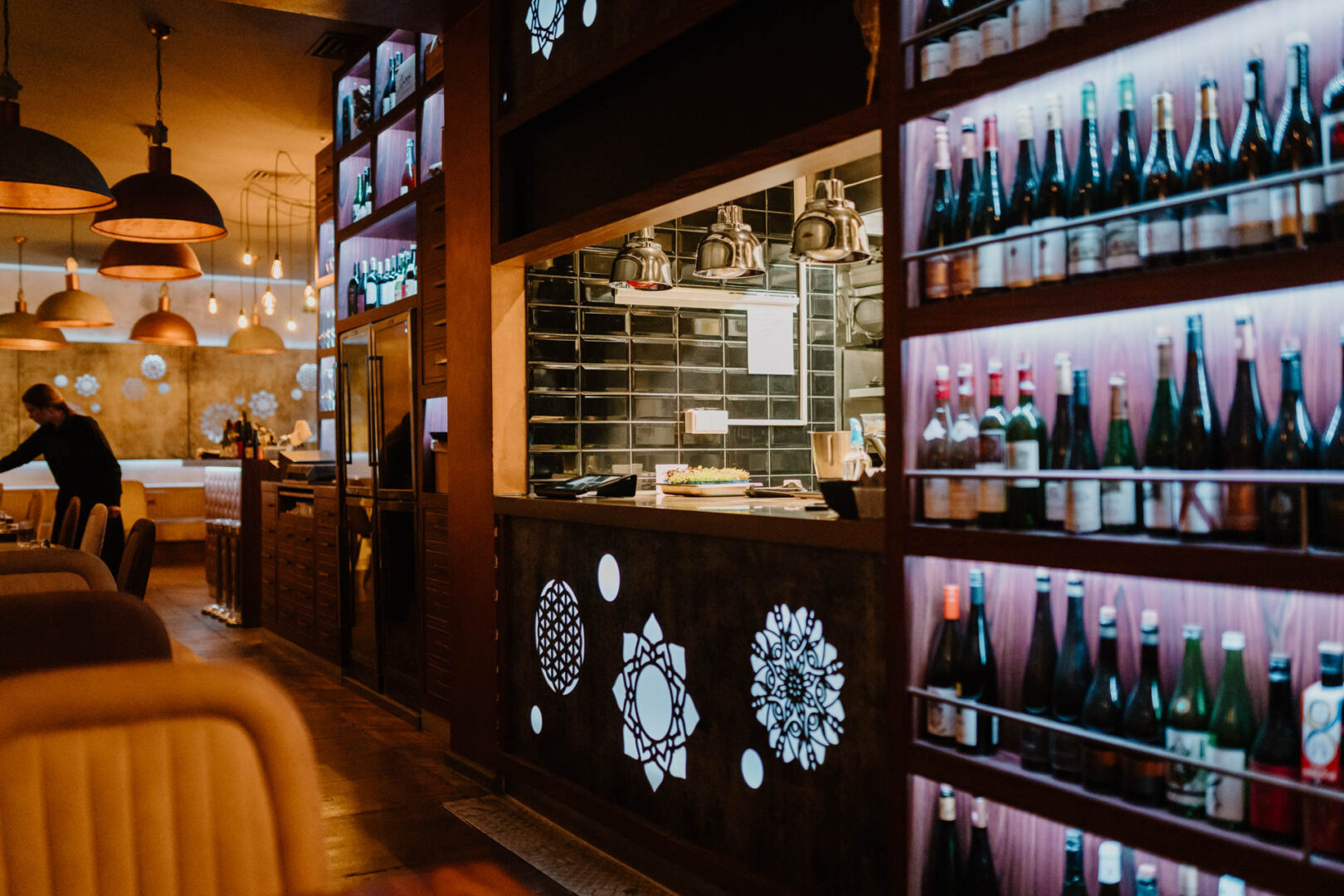 Man sieht das Sushi Lokal Roku von innen. Rechts ein Kühlregal voller Sake-Flaschen, links davon eine beleuchtete Bar und links vom Gang Tische und Stühle.