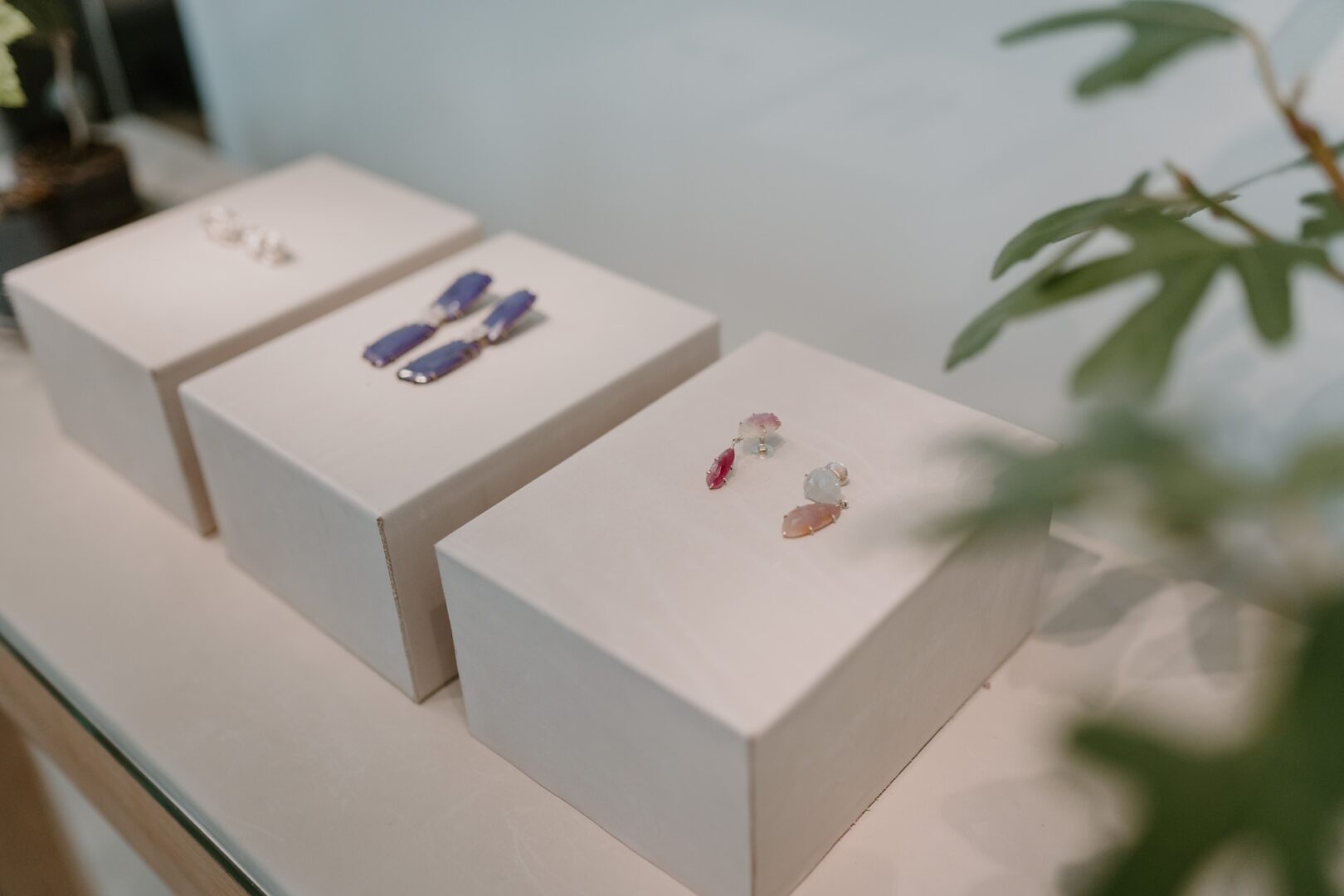 Man sieht die drei helle, kleine Blöcke in einer Vitrine. Auf jedem Block ist ein paar Ohrringe arrangiert.