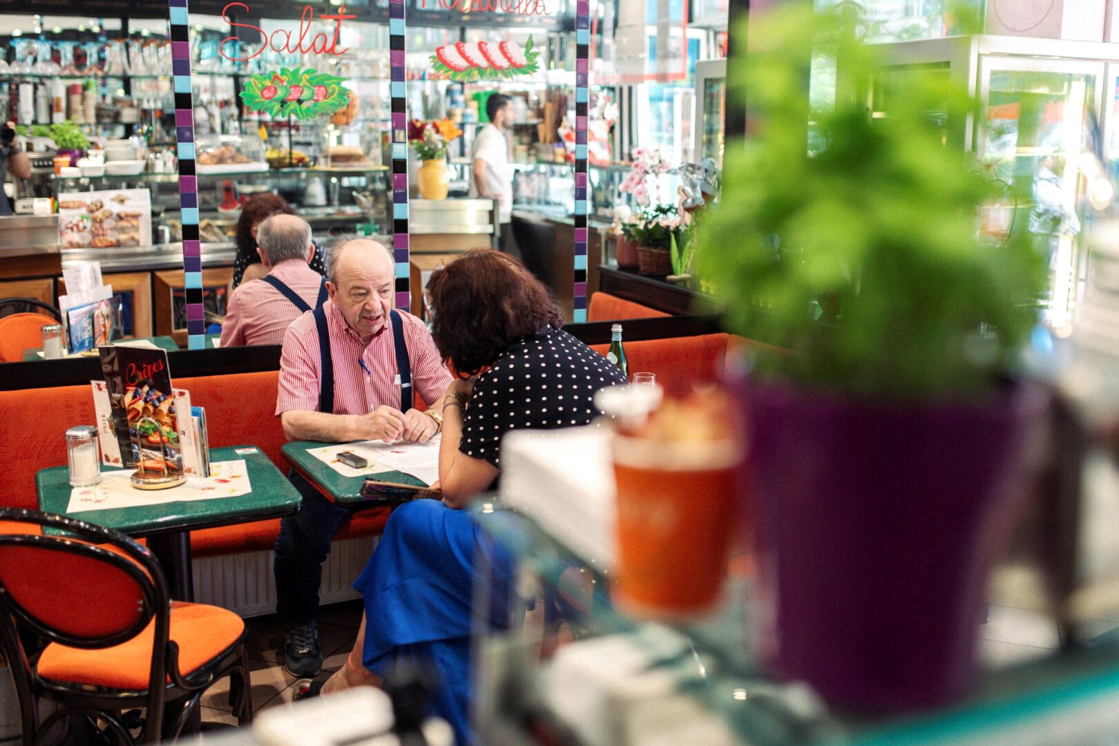 Roberto sitzt in seiner Eisdiele an einem kleinen Bistrotisch, hinter ihm ein langer Spiegel, der sich durch den ganzen Raum zu ziehen scheint.