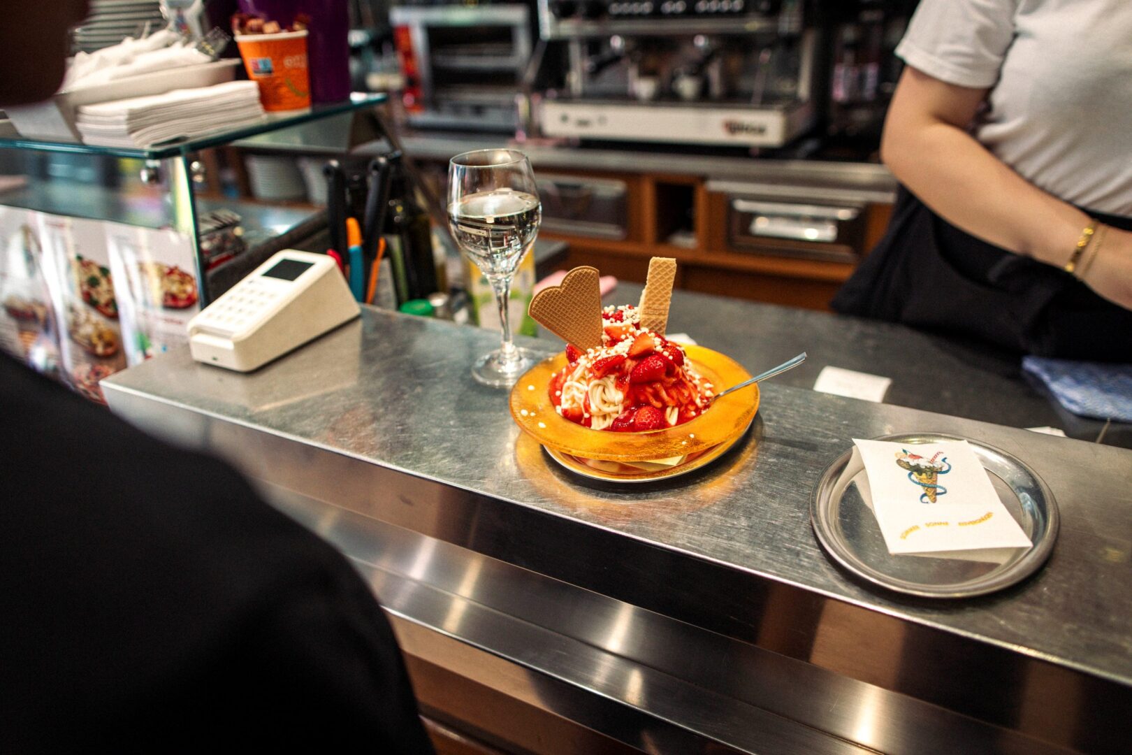 Man sieht ein STück des Tresens aus blank poliertem Edelstahl und darauf ein Spaghettieis mit frischen Erdbeeren.