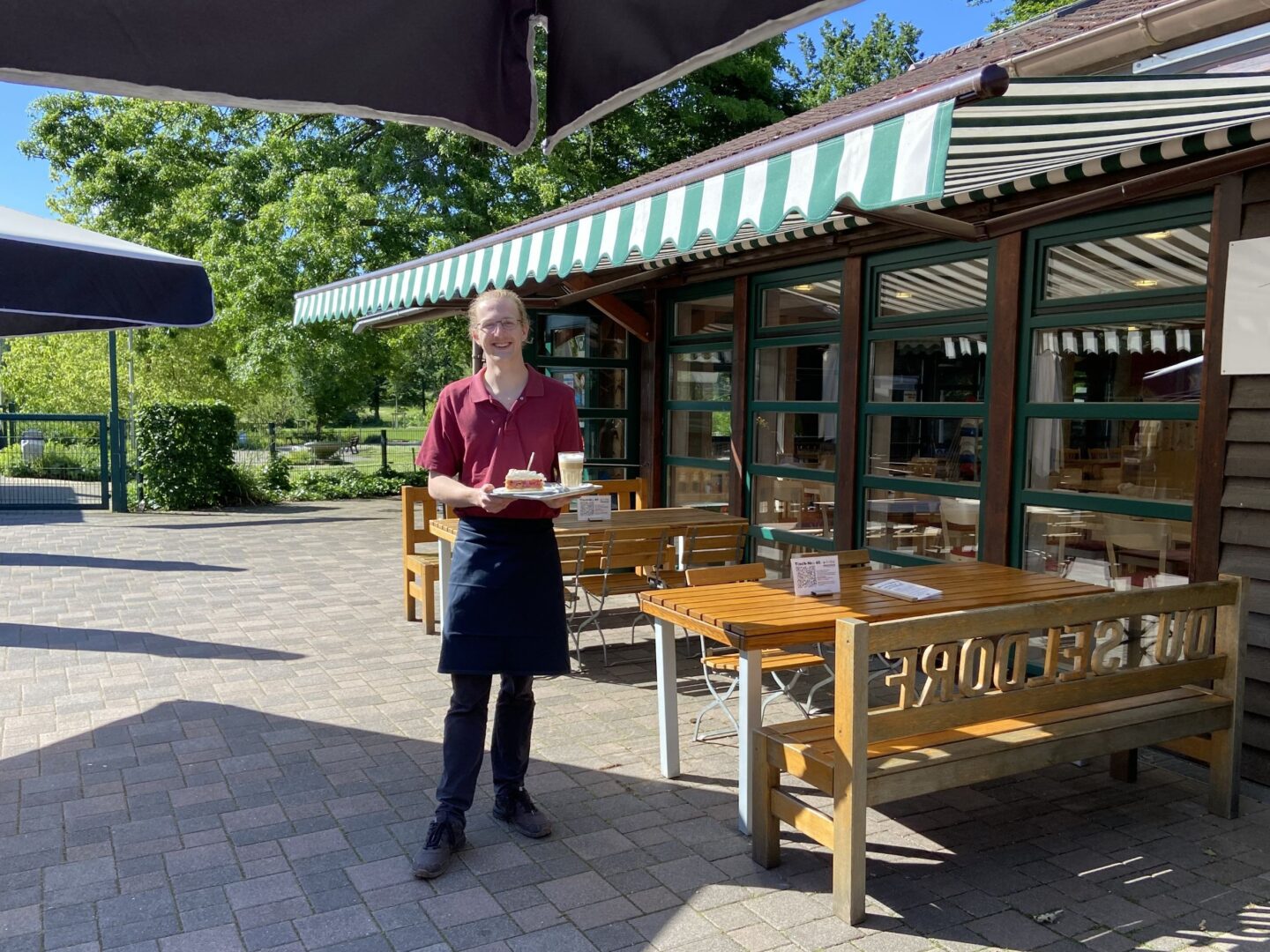 Man sieht eine Servicekraft mit einem Tablett auf der Terrasse des Café Südpark.