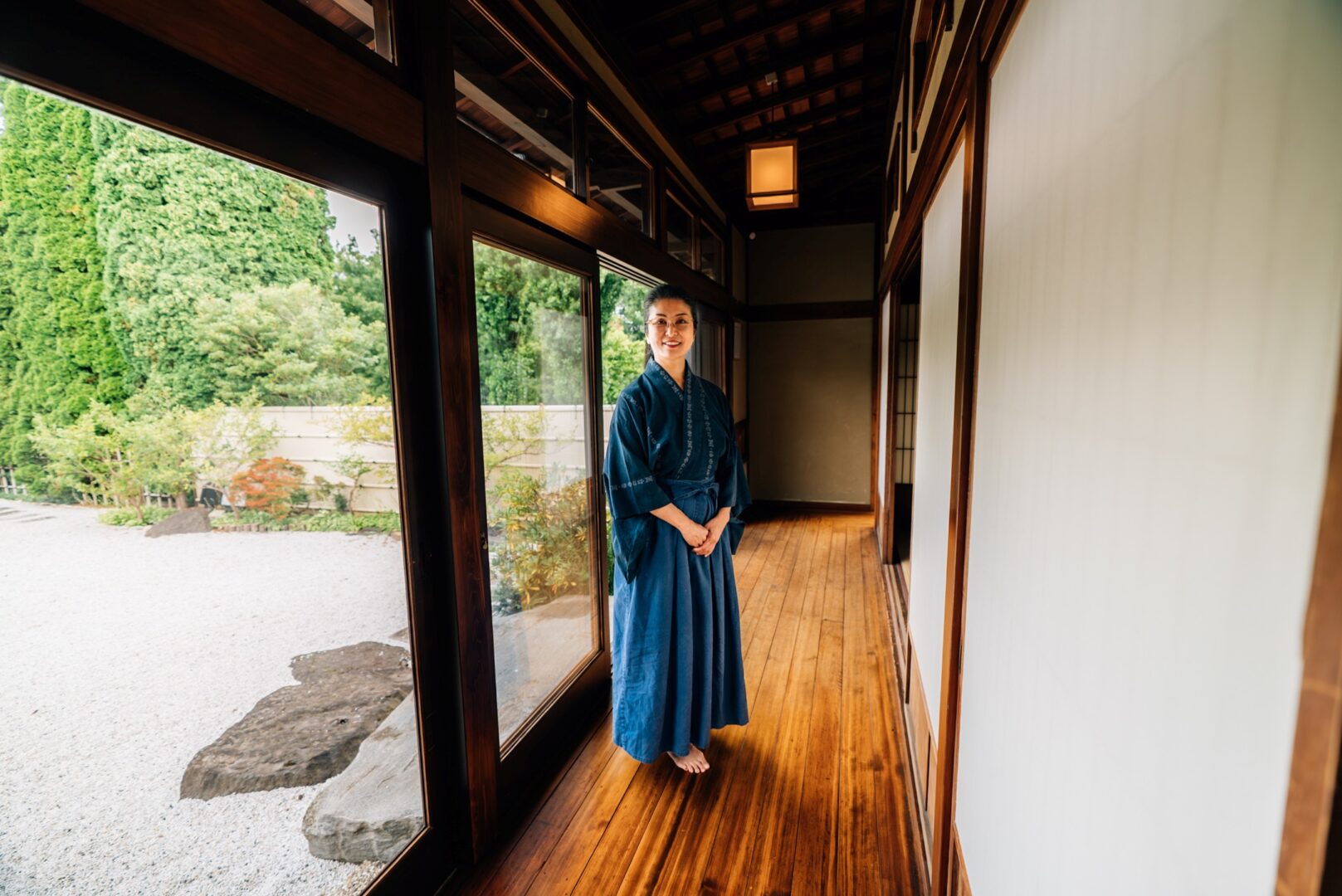 Aya Murakami in einem Gang des EKO-Hauses. Bodentiefe Fenster führen zum Garten. Der Boden des Gangs ist aus Holz.
