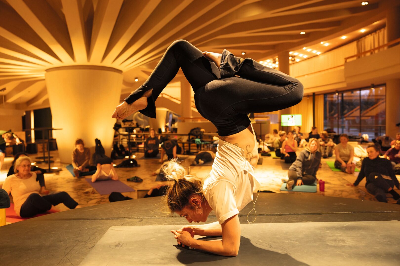 Man sieht im Foyer im Düsseldorfer Schauspielhaus eine Person auf einer kleinen Bühne, die eine Art Unterarmhandstand macht.