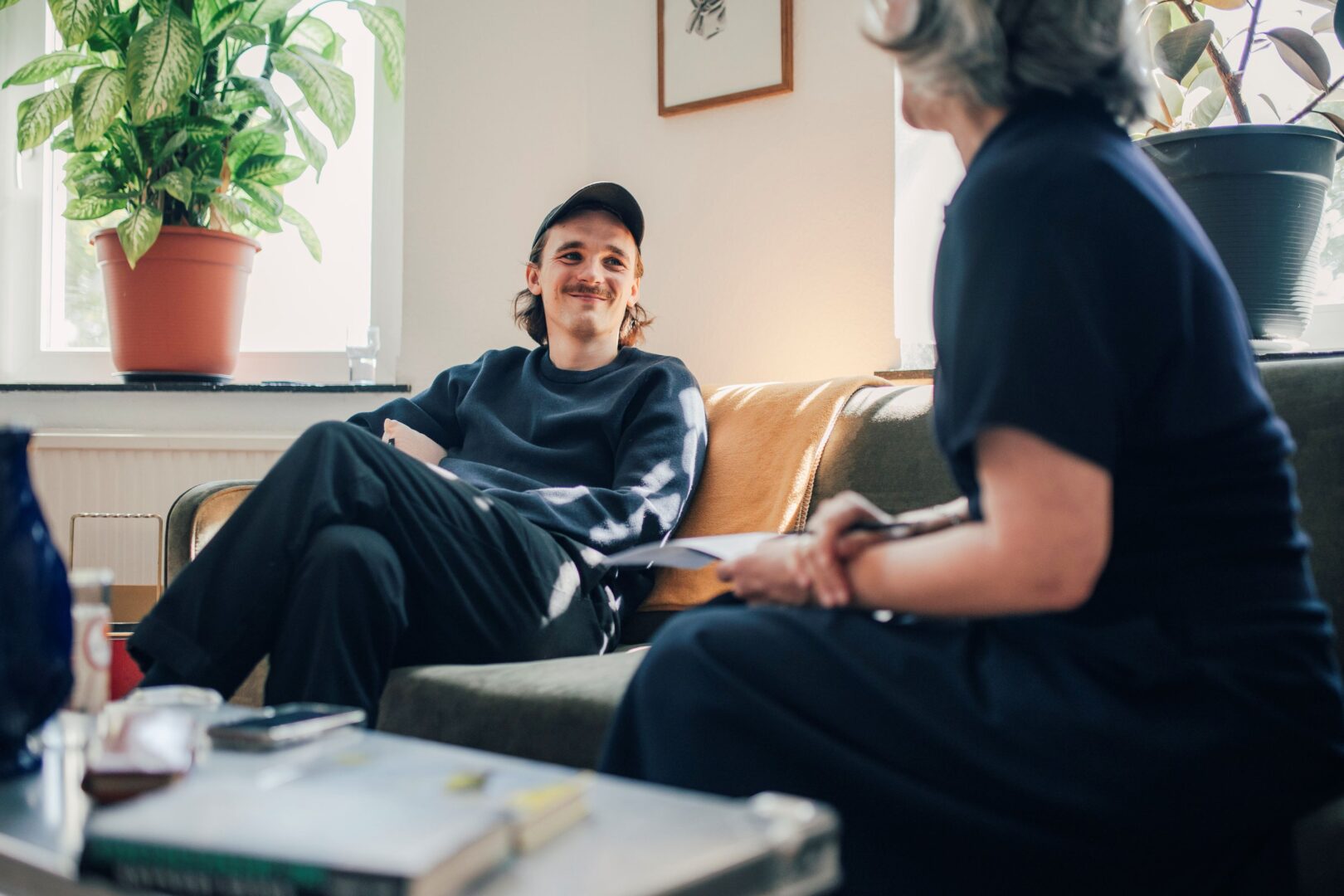 Kaleb Erdmann sitzt auf seinem Sofa, während des Interviews. Rechts sieht man die Autorin unscharf im Anschnitt.