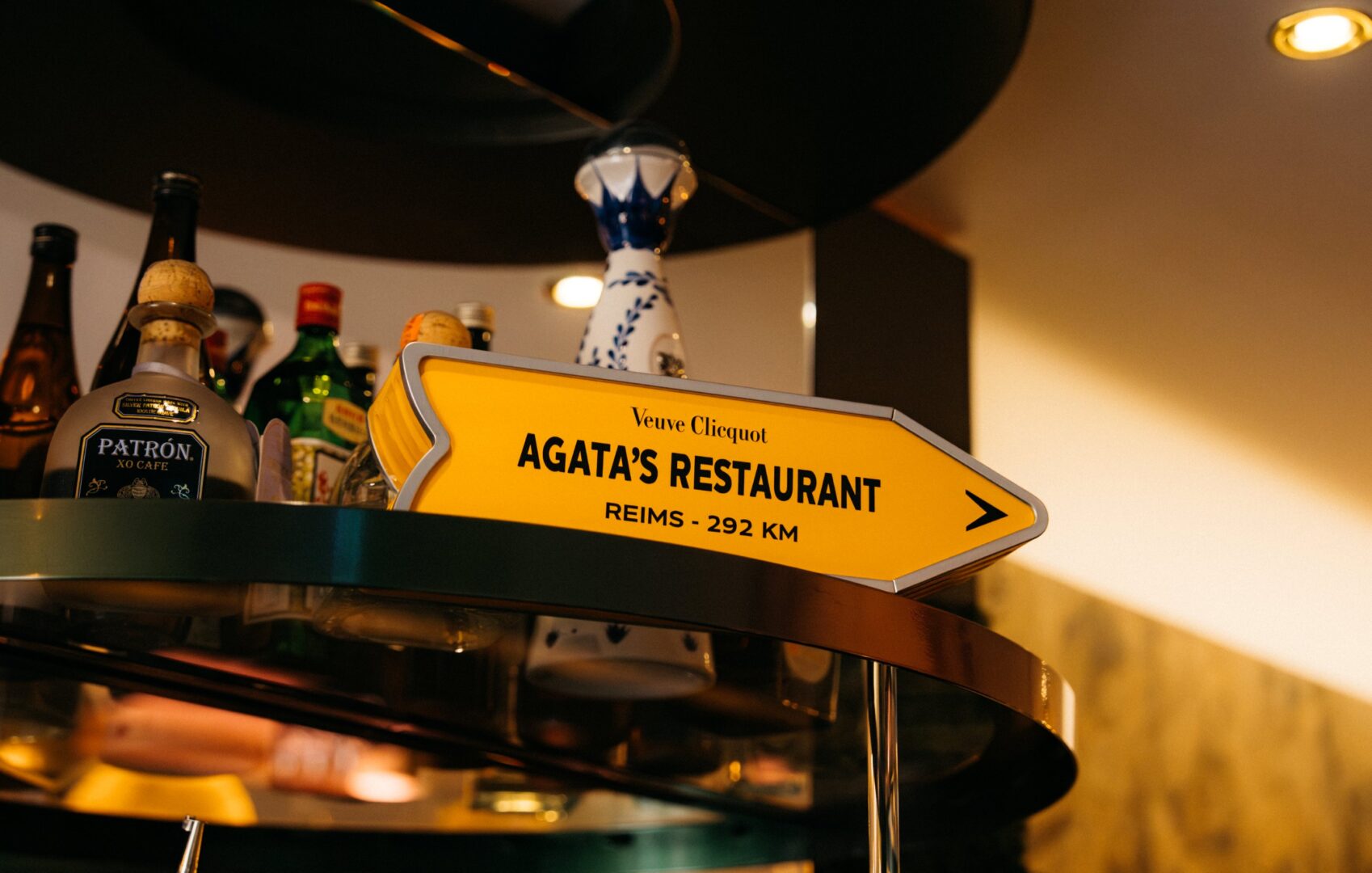 Ein orangefarbenes Schild, das wie ein gelbes Umleitungsschild gestaltet ist, auf dem steht: Agata's Restaurant, Reims 292 km.