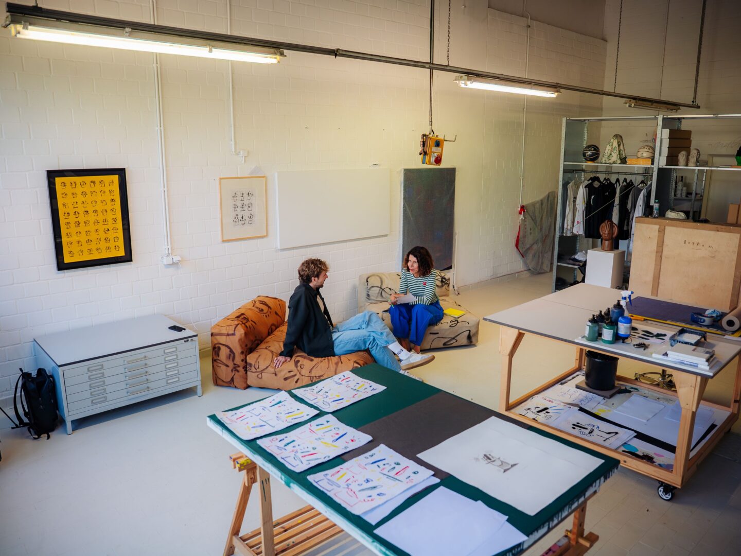 Weitwinkelaufnahme im Atelier beim Interview. Man sieht einen großen Schreibtisch mit Illustrationen im Vordergrund und dahinter Steffen Mumm und Ilona Marx im Gespräch.