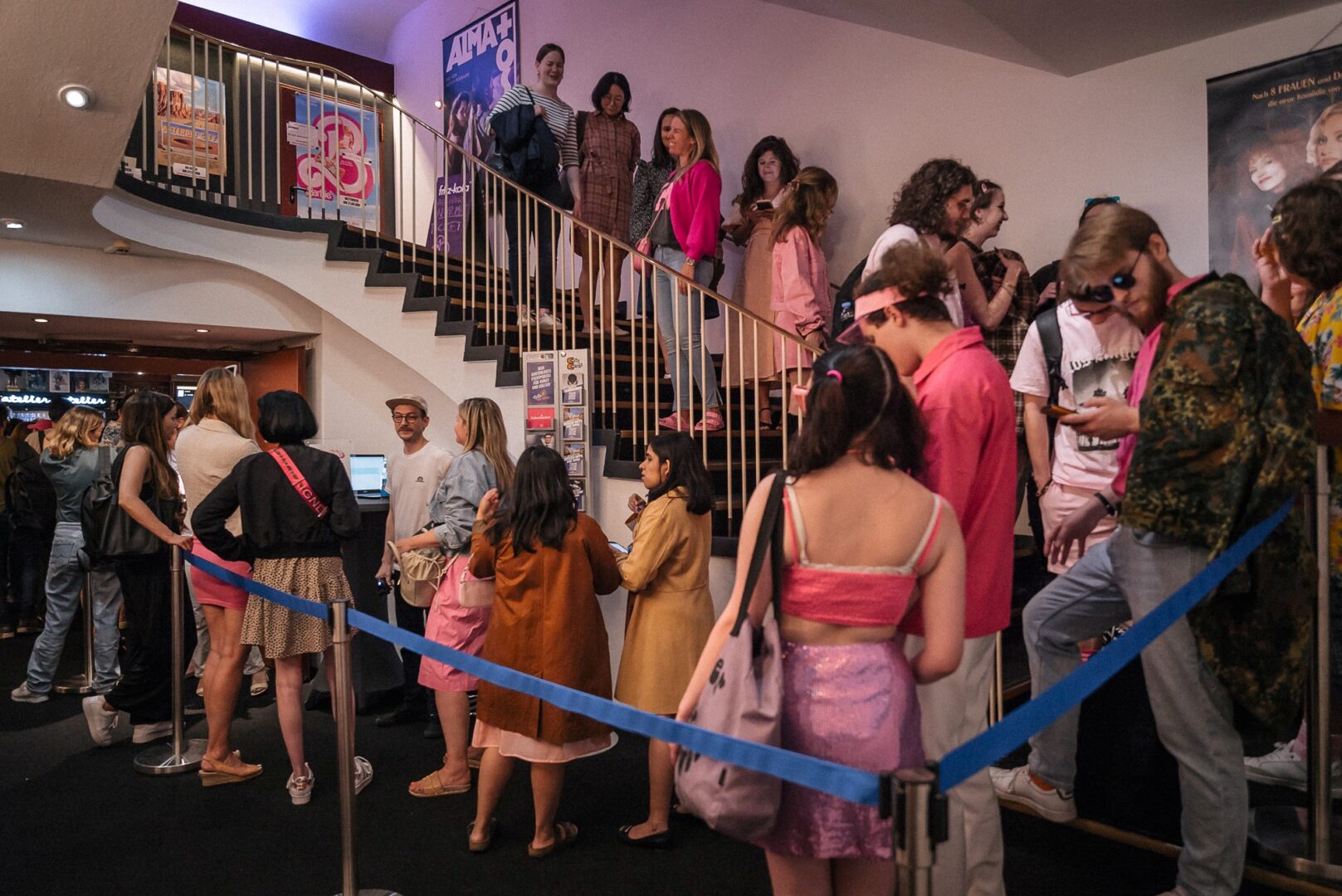 Man sieht eine Menschenschlange, die auf einer geschwungenen Treppe stehen und zur Vorpremiere des Films "Barbie" möchten.