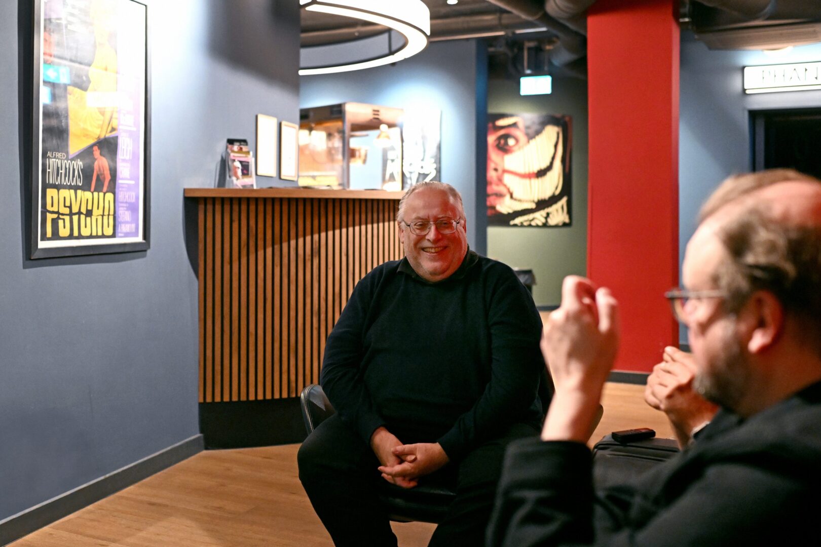 Man sieht Kalle frontal aufgenommen ganz in Schwarz gekleidt im Foyer des Metropol im Interview, rechts angeschnitten eine Hand.