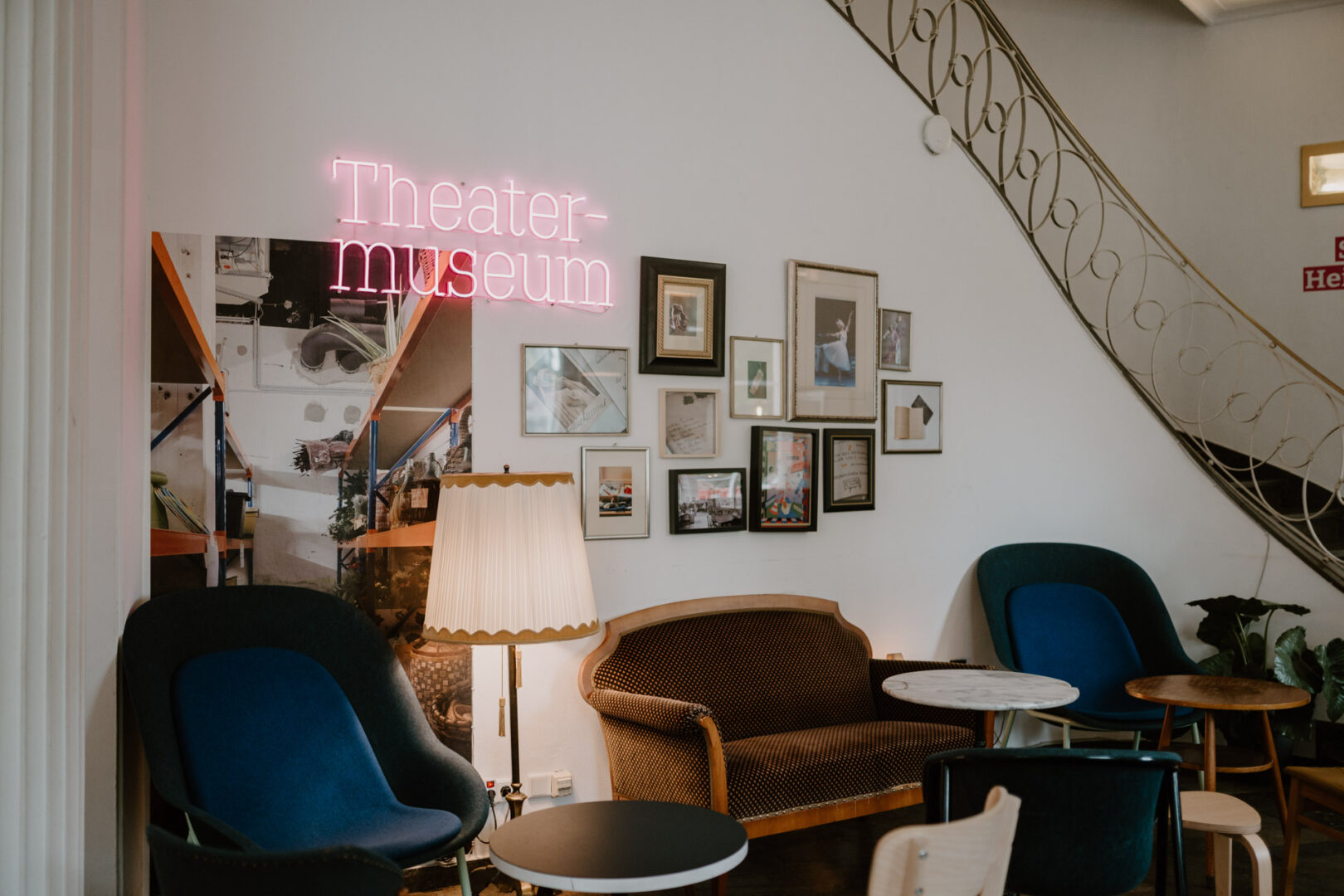 Das Foyer mit Sesseln und gerahmten Bildern im Midcentury-Stil. Zentral hängt ein Neonschriftzug "Theatermuseum".