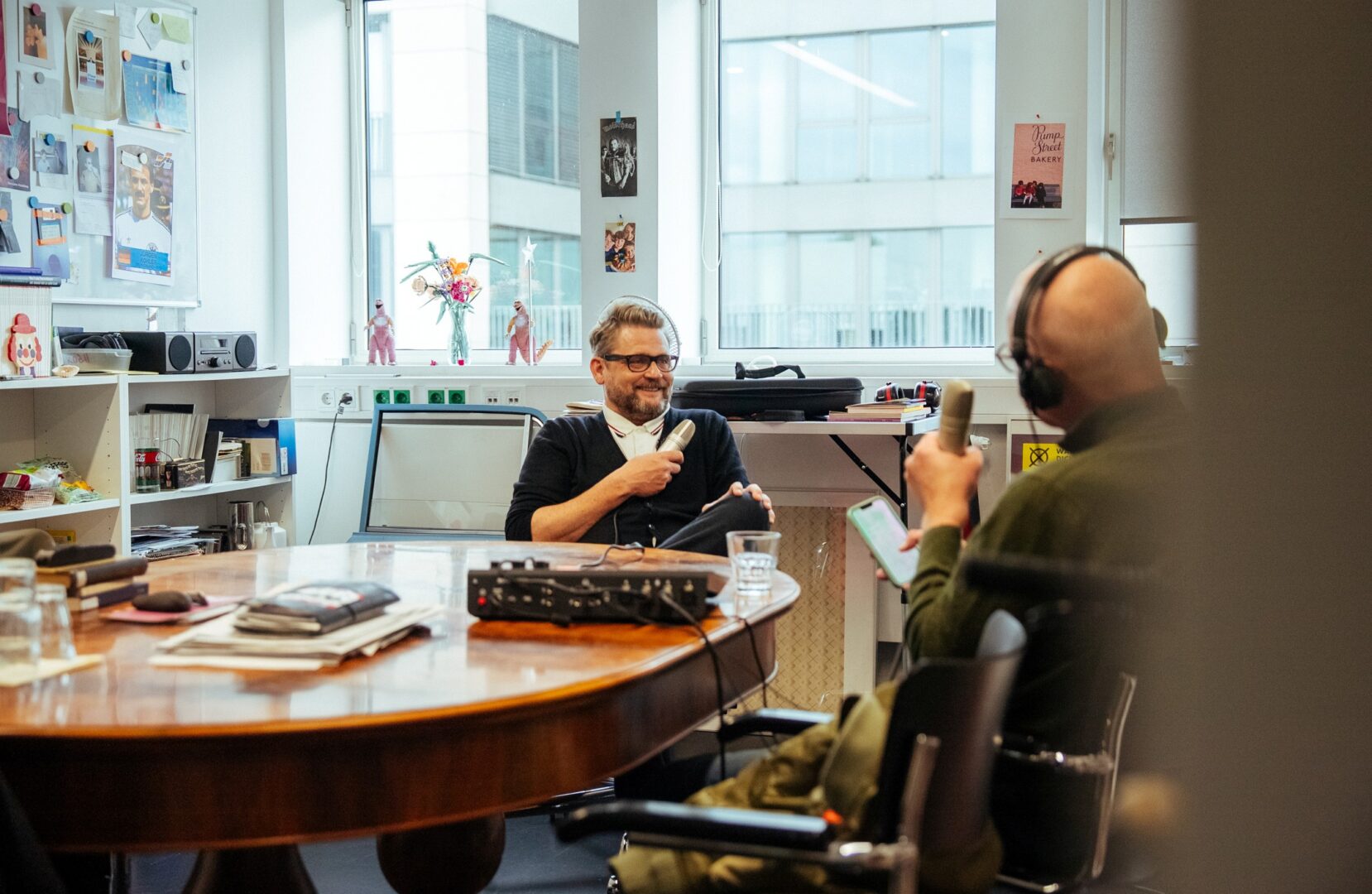 Robert Koall und Mike Litt sitzen im Büro von Koall an einem Holztisch und nehmen den Podcast auf.
